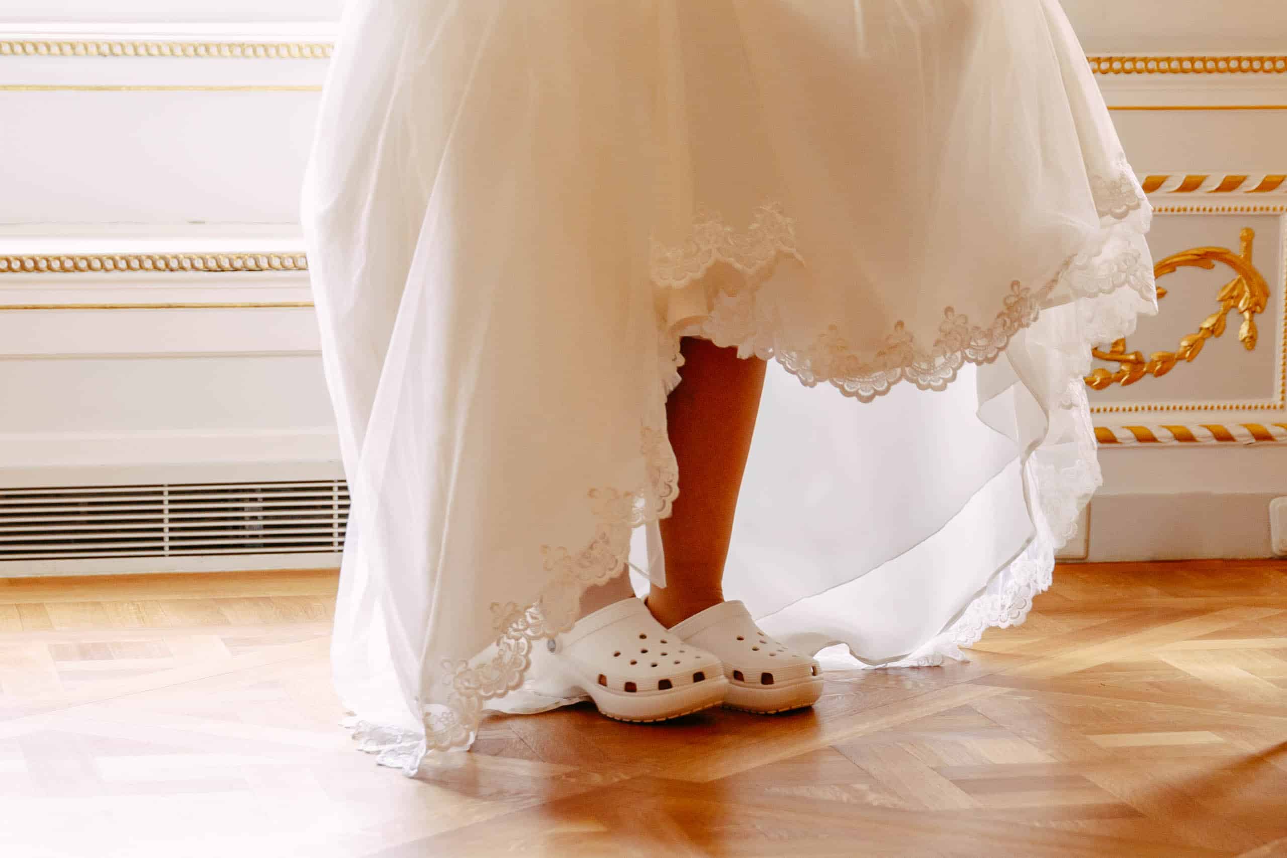 Een bruid in een witte jurk staat op een houten vloer en draagt comfortabele bruidsschoenen.