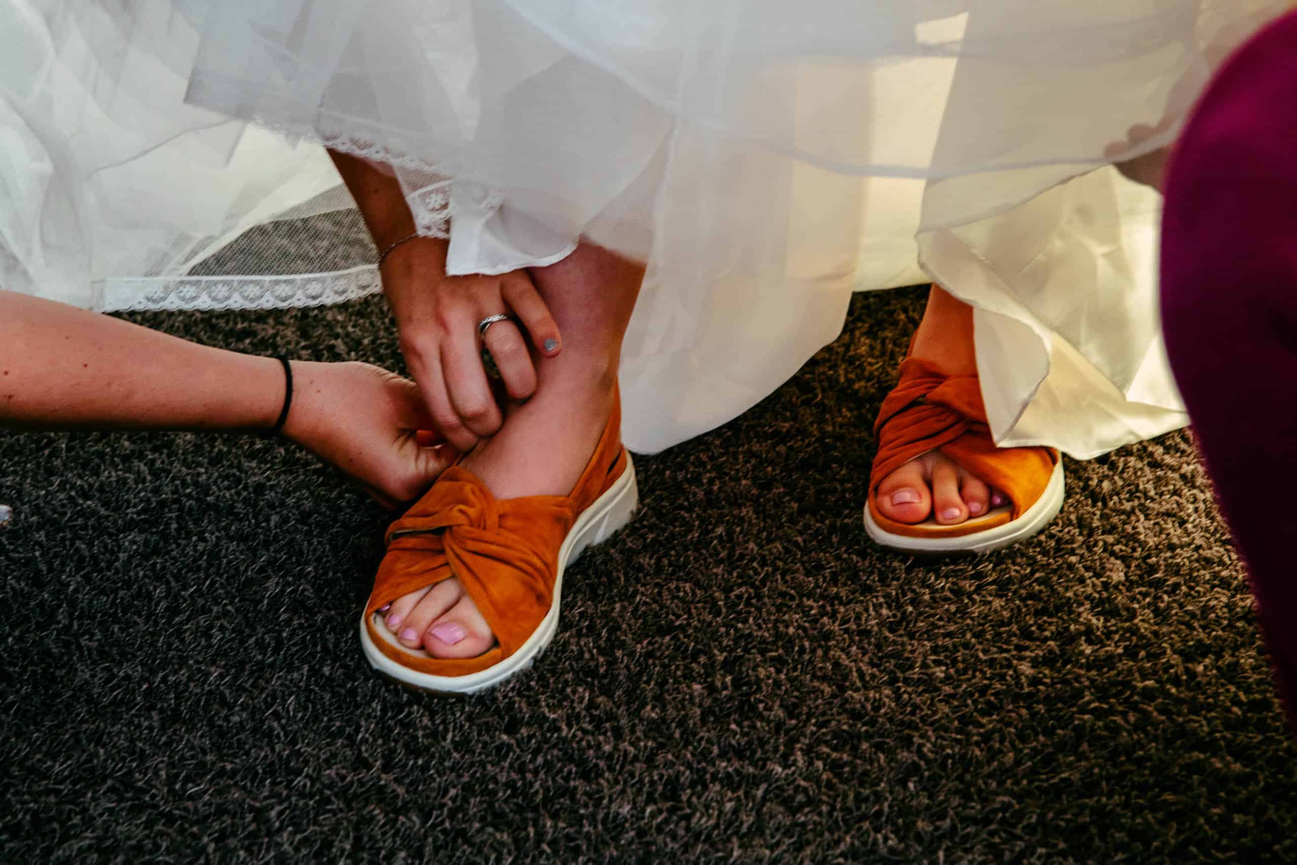 Een bruid die comfortabel haar bruidsschoenen in een trouwjurk vastbindt.