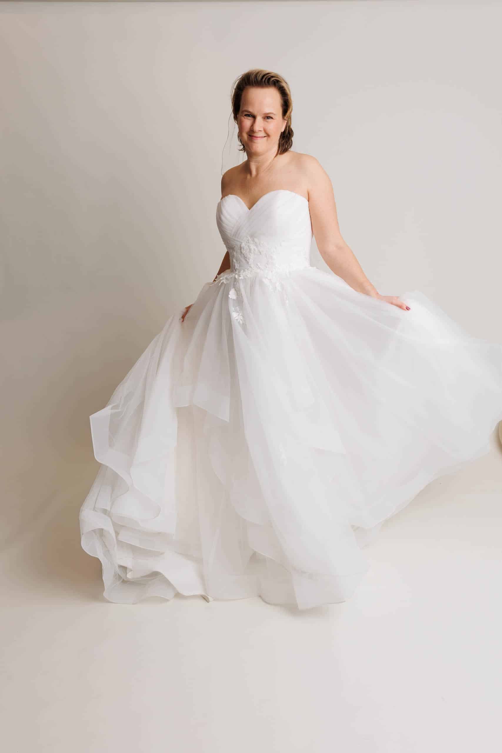 A woman in a white wedding dress poses for a photo while trying on different wedding dresses for fun.