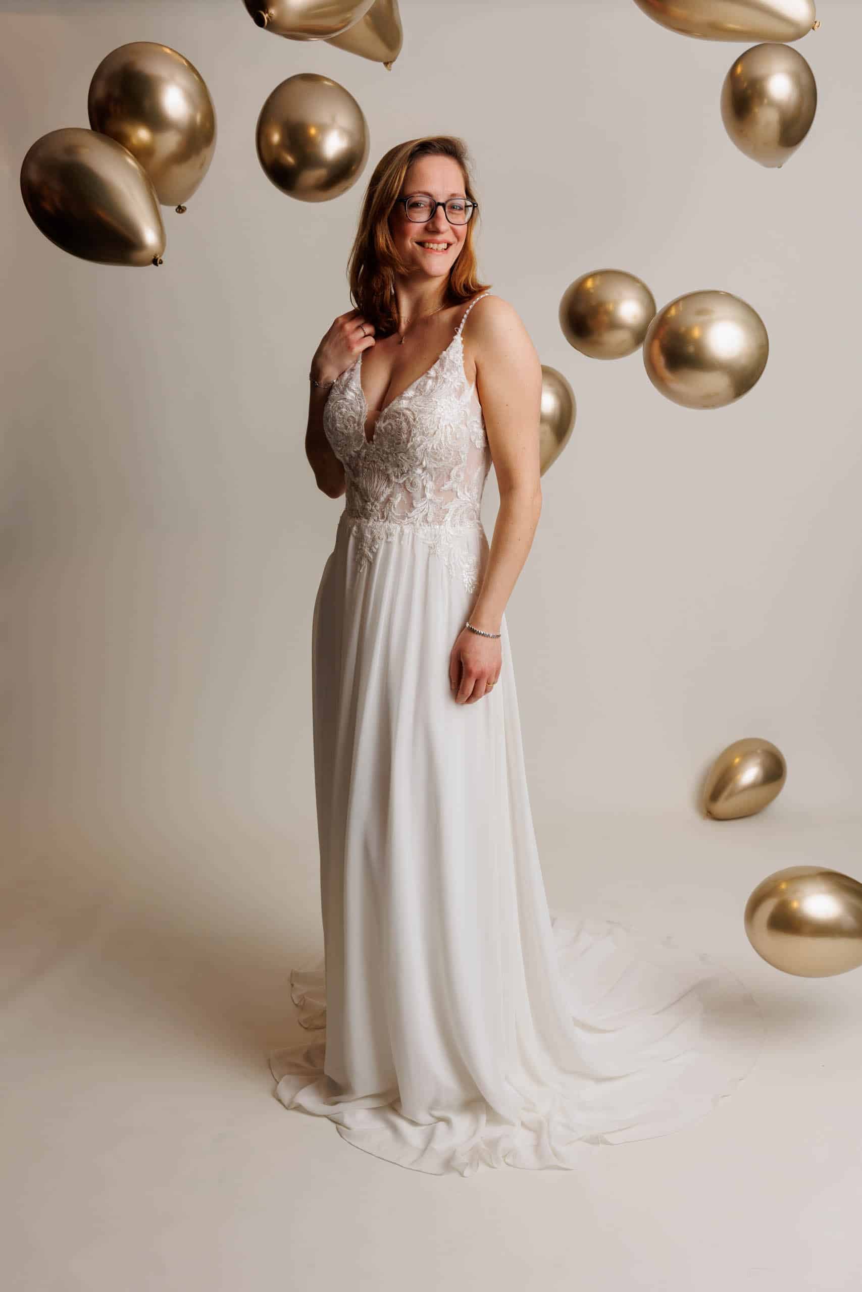 Een vrouw die voor de lol trouwjurken past, poserend voor gouden ballonnen.