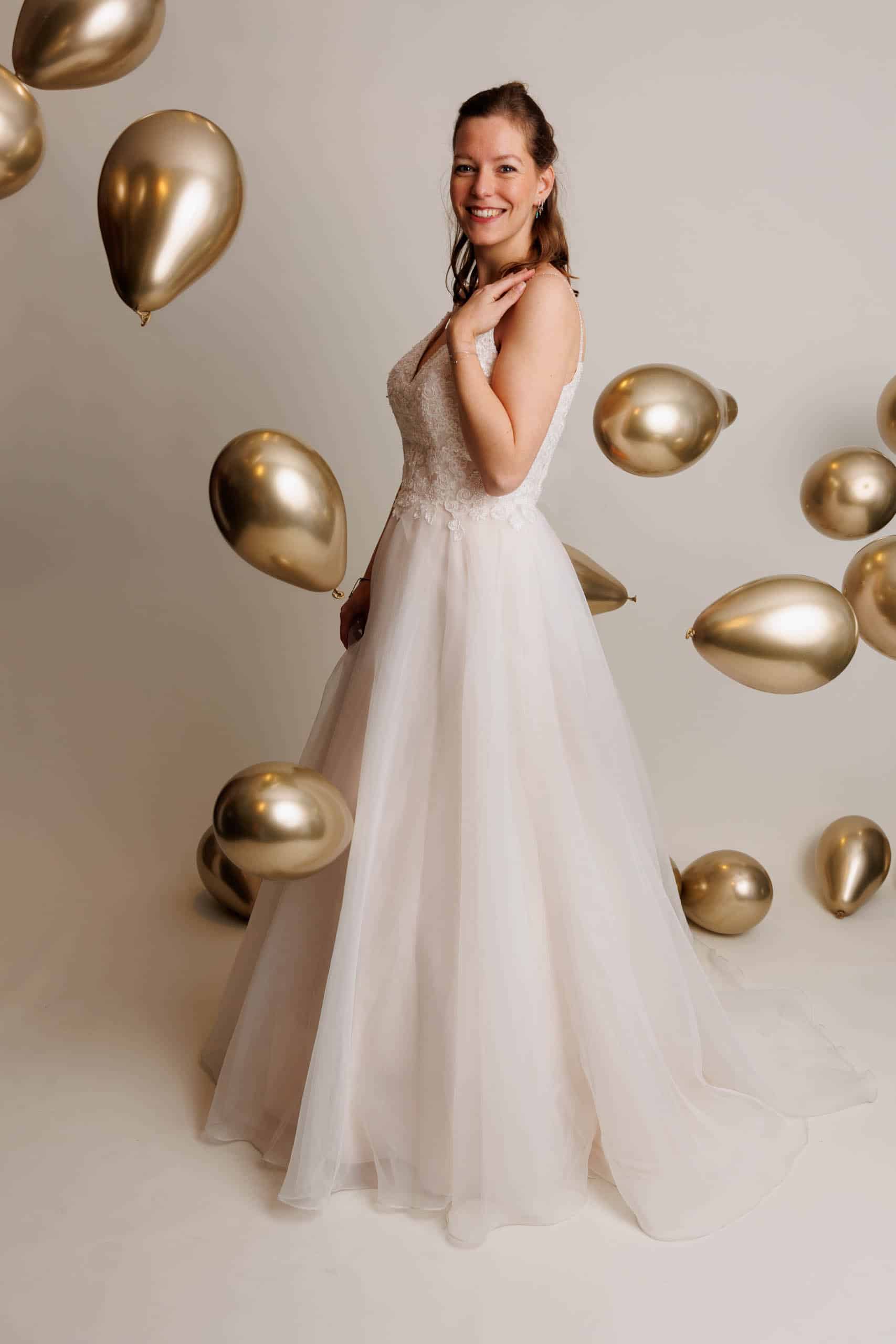 A woman in a wedding dress surrounded by golden balloons, enjoying the fun of trying on different wedding dresses.