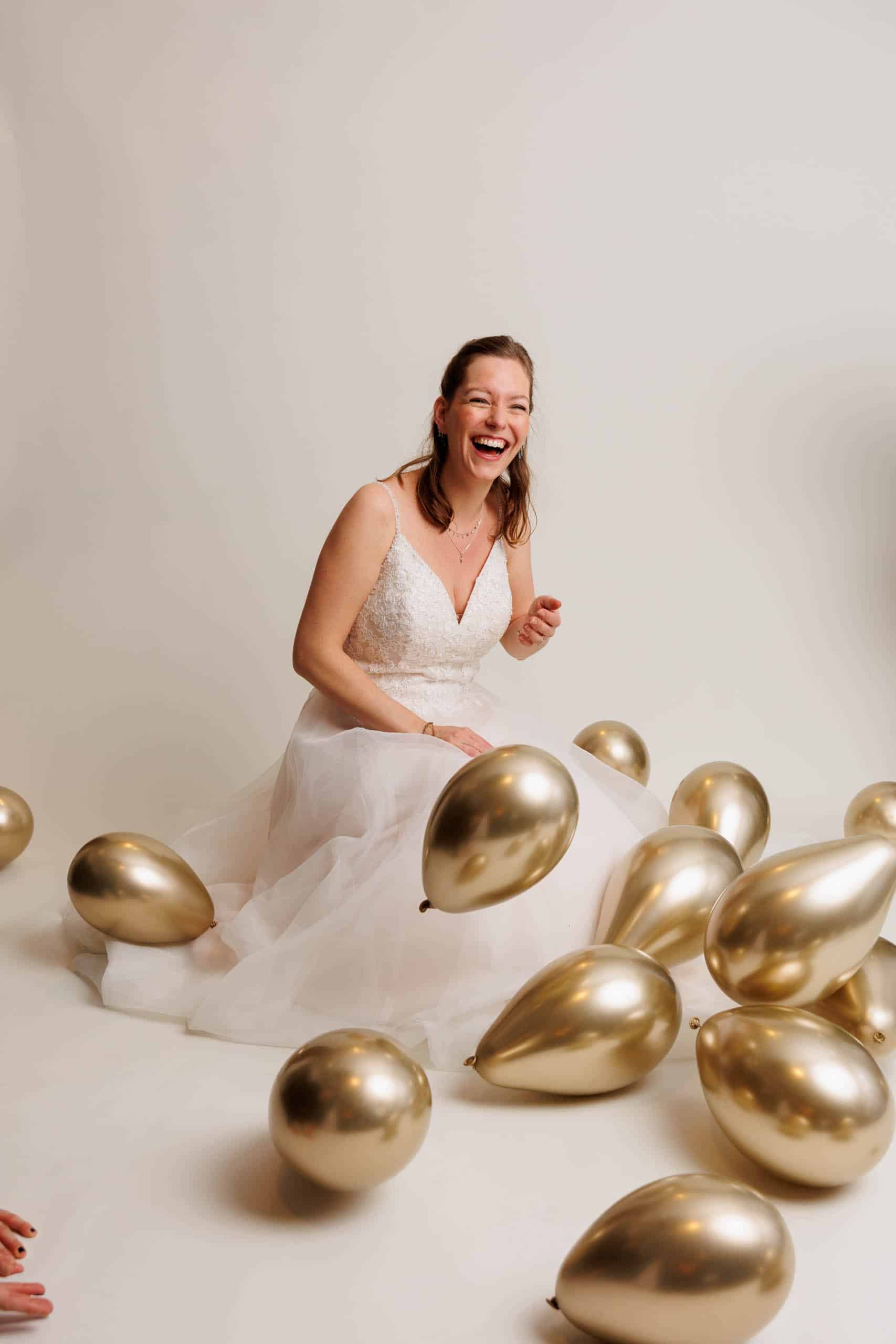 Beschrijving: Een bruid in een witte trouwjurk met gouden ballonnen om haar heen.