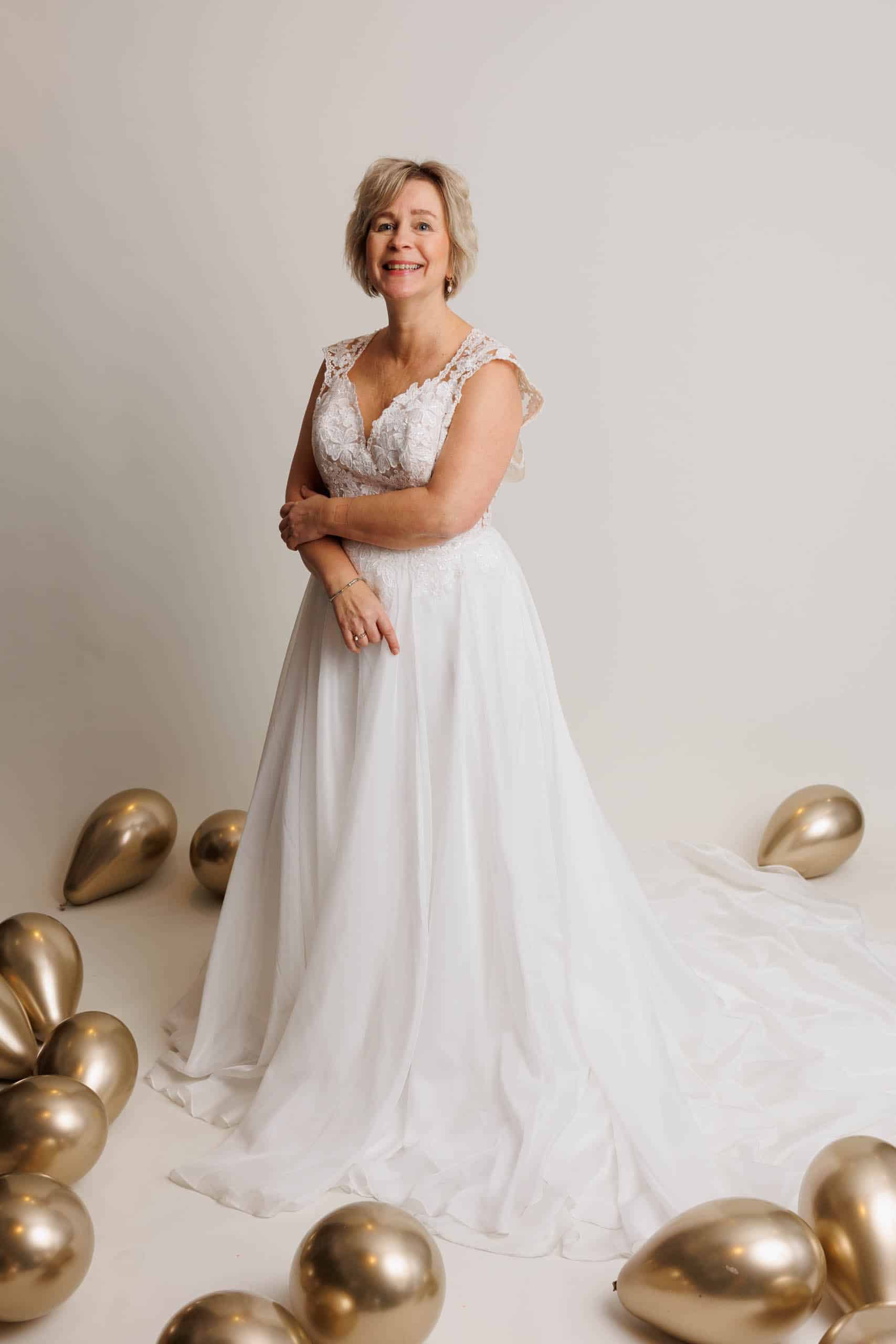 A woman in a wedding dress poses in front of gold balloons while trying on wedding dresses for fun.