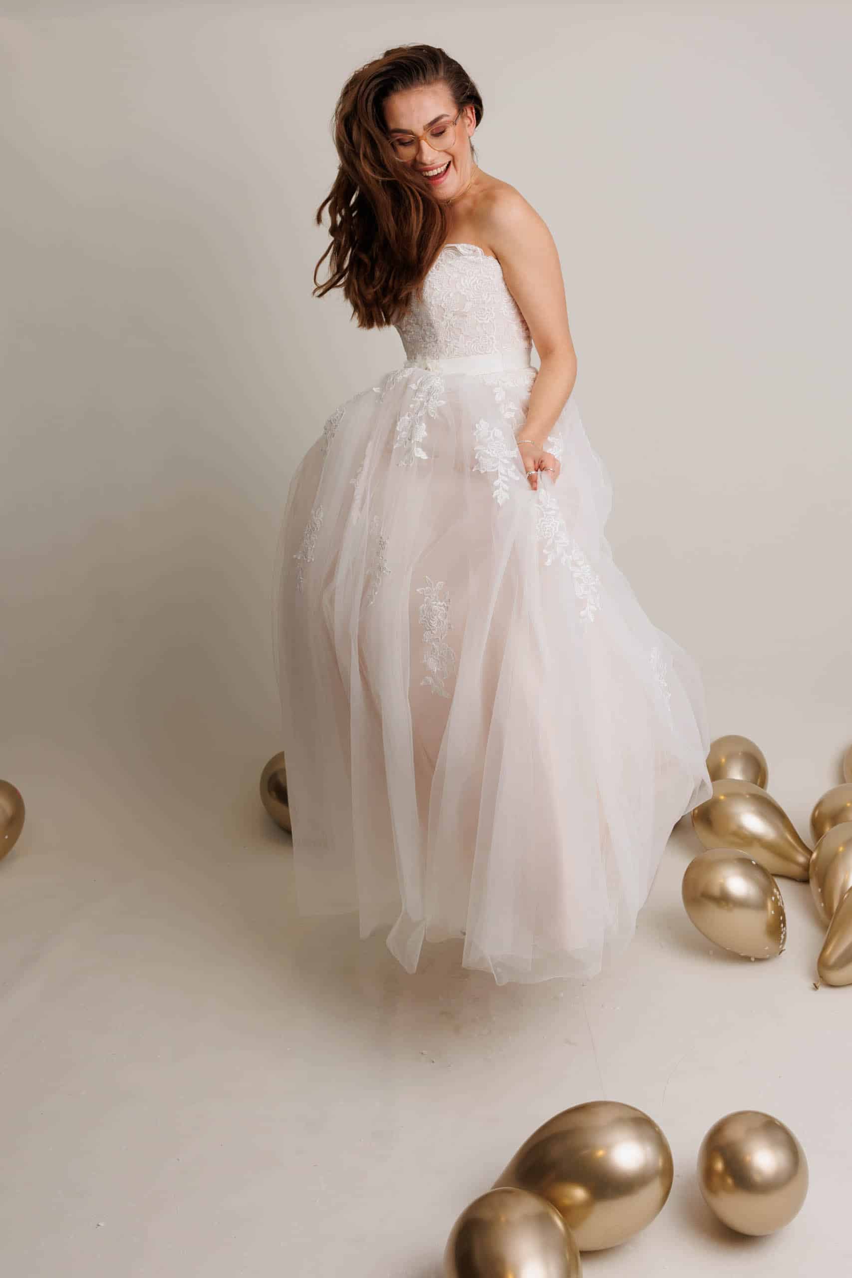 A bride in a wedding dress poses in front of gold balloons while trying on wedding dresses for fun.