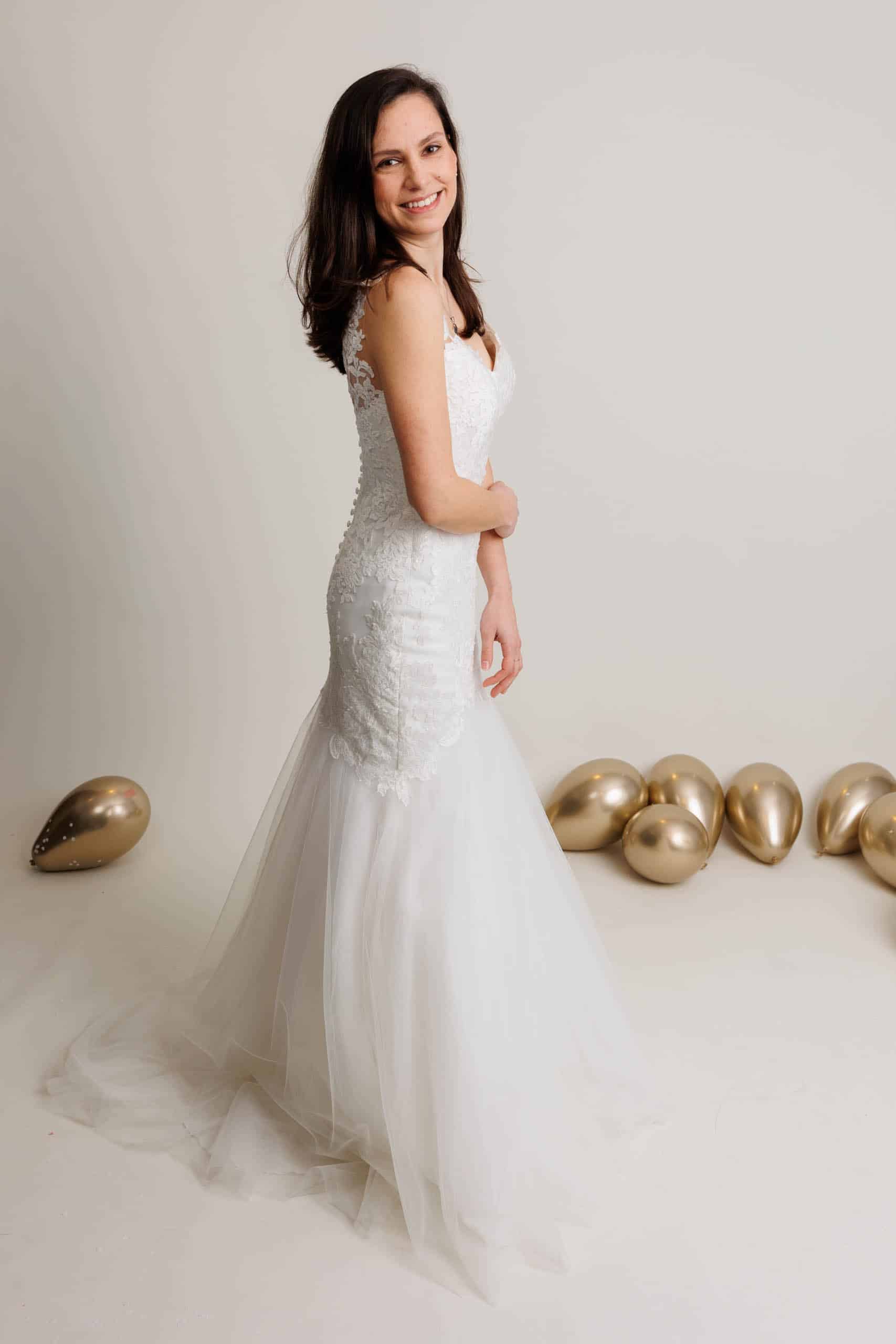 A bride in a wedding dress poses in front of gold balloons while trying on wedding dresses.