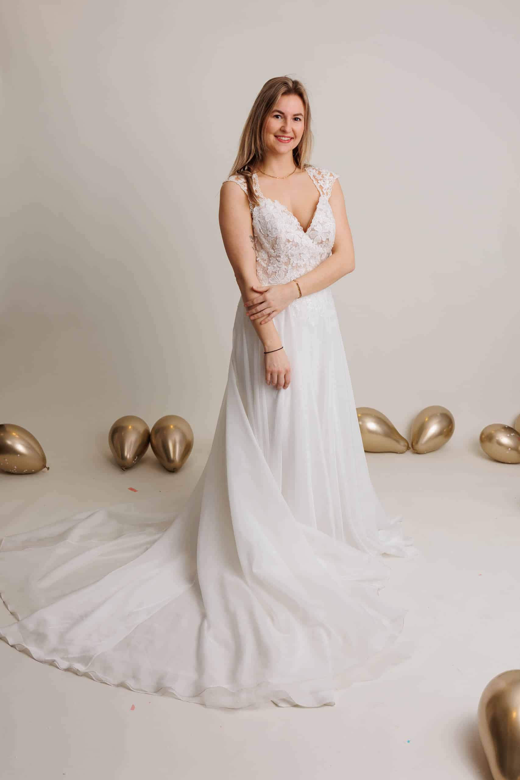 A woman in a white wedding dress poses in front of balloons while trying on wedding dresses for fun.