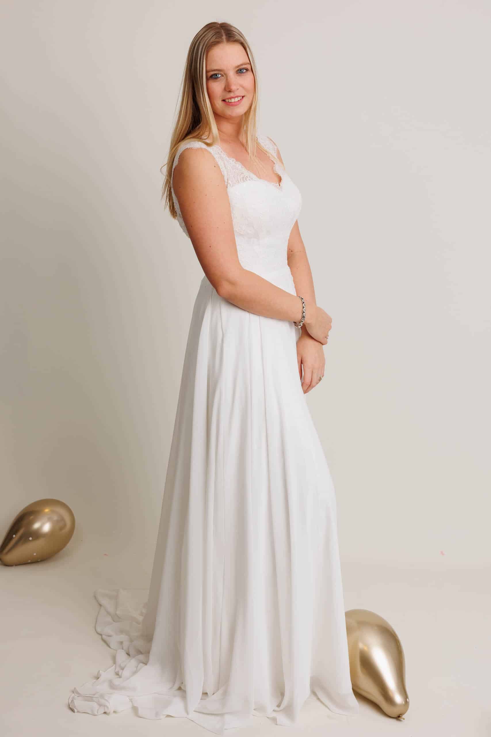 A woman in a white wedding dress poses with gold balloons.
