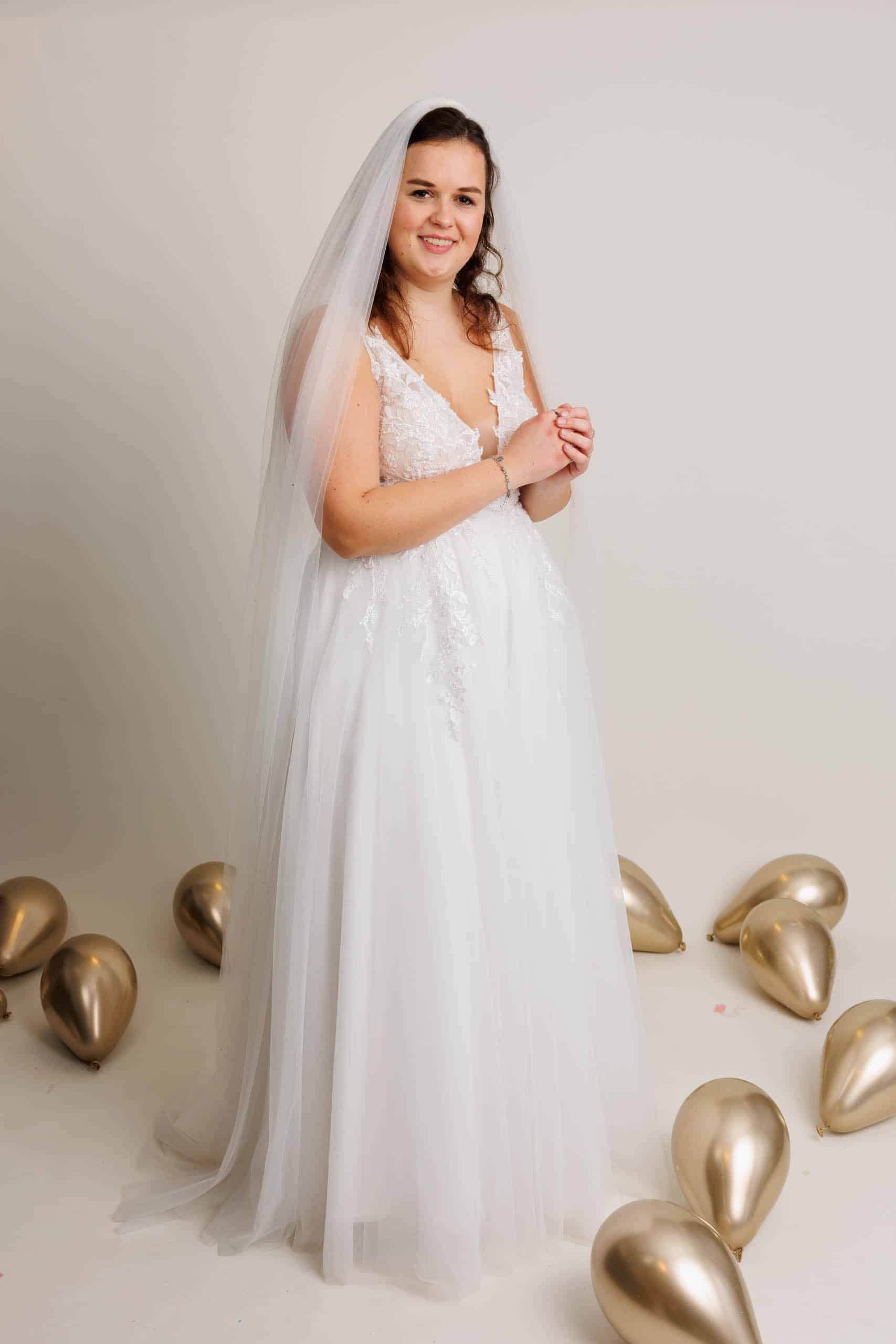 A woman in a wedding dress poses in front of balloons while trying on wedding dresses for fun.