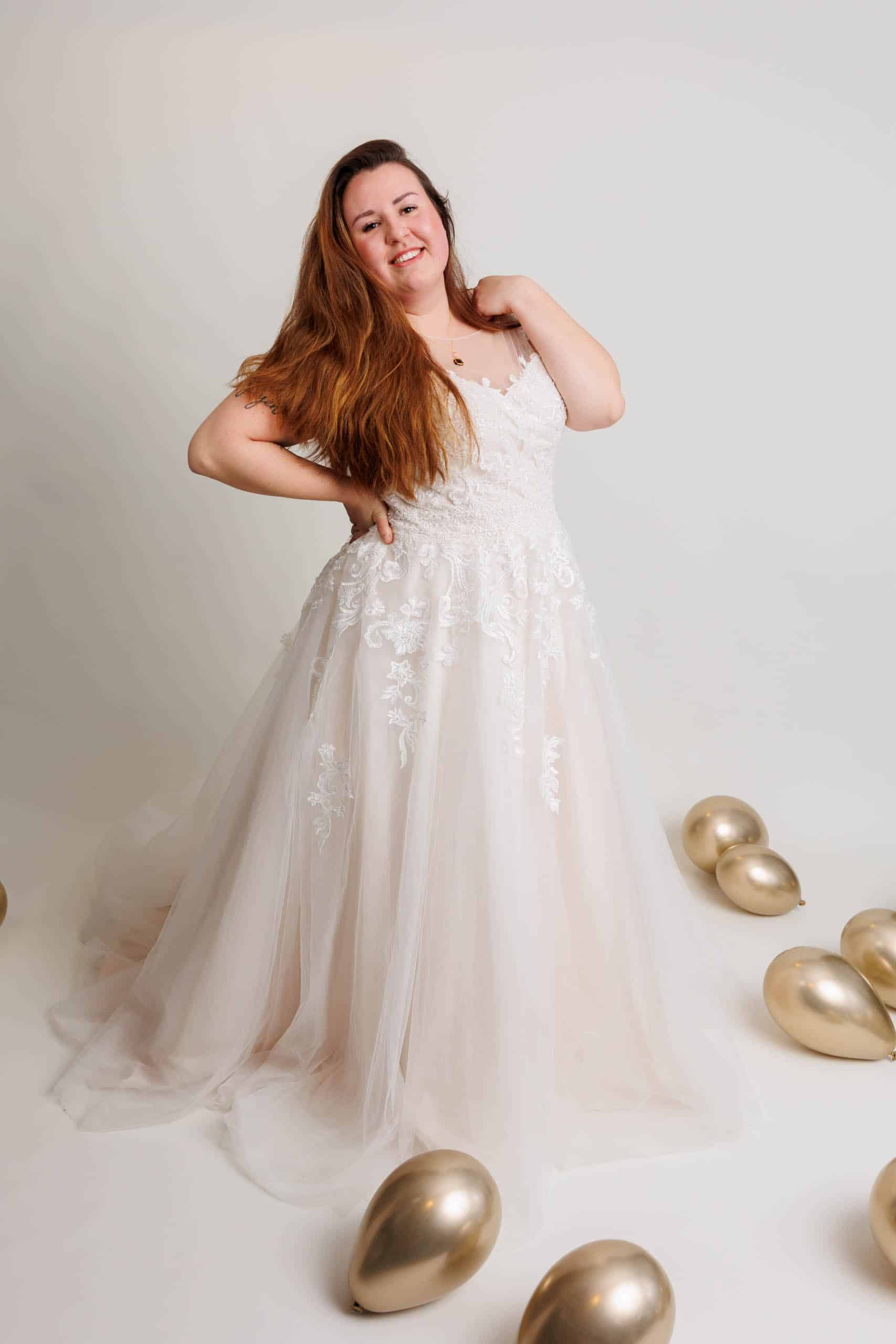A woman in a wedding dress poses with gold balloons while trying on wedding dresses for fun.