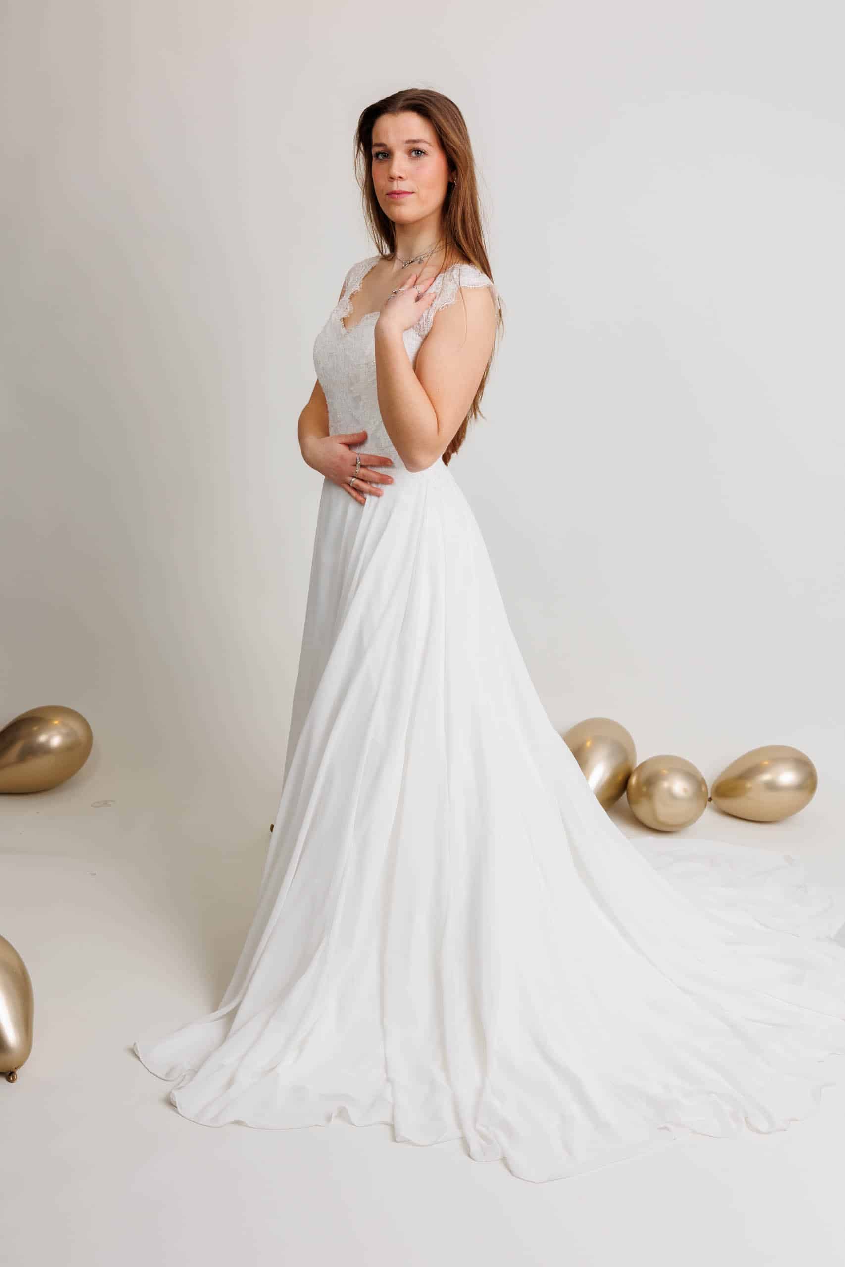 A woman in a white wedding dress poses with gold balloons while trying on wedding dresses for fun.