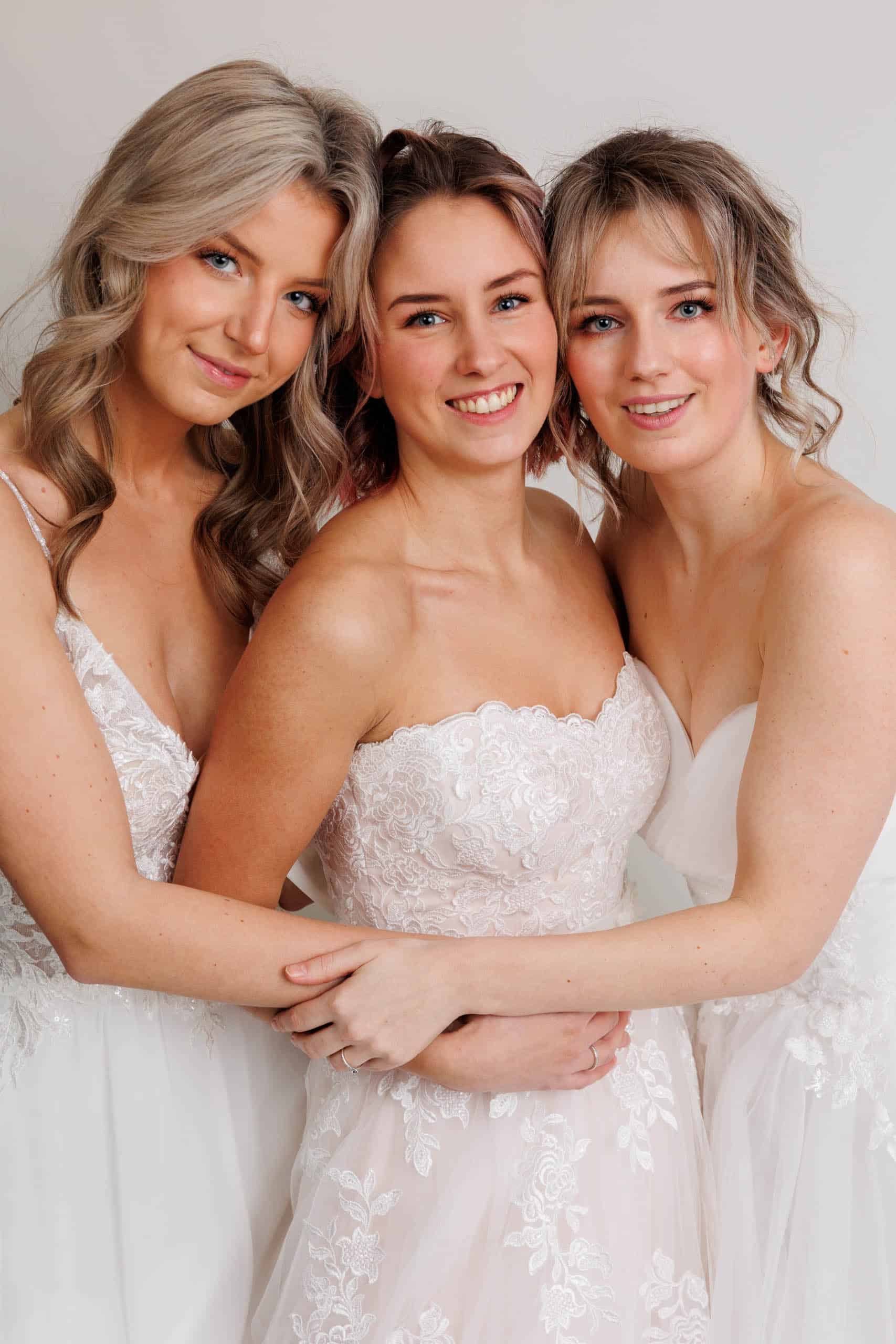 Three bridesmaids try on wedding dresses for fun while posing for a photo.
