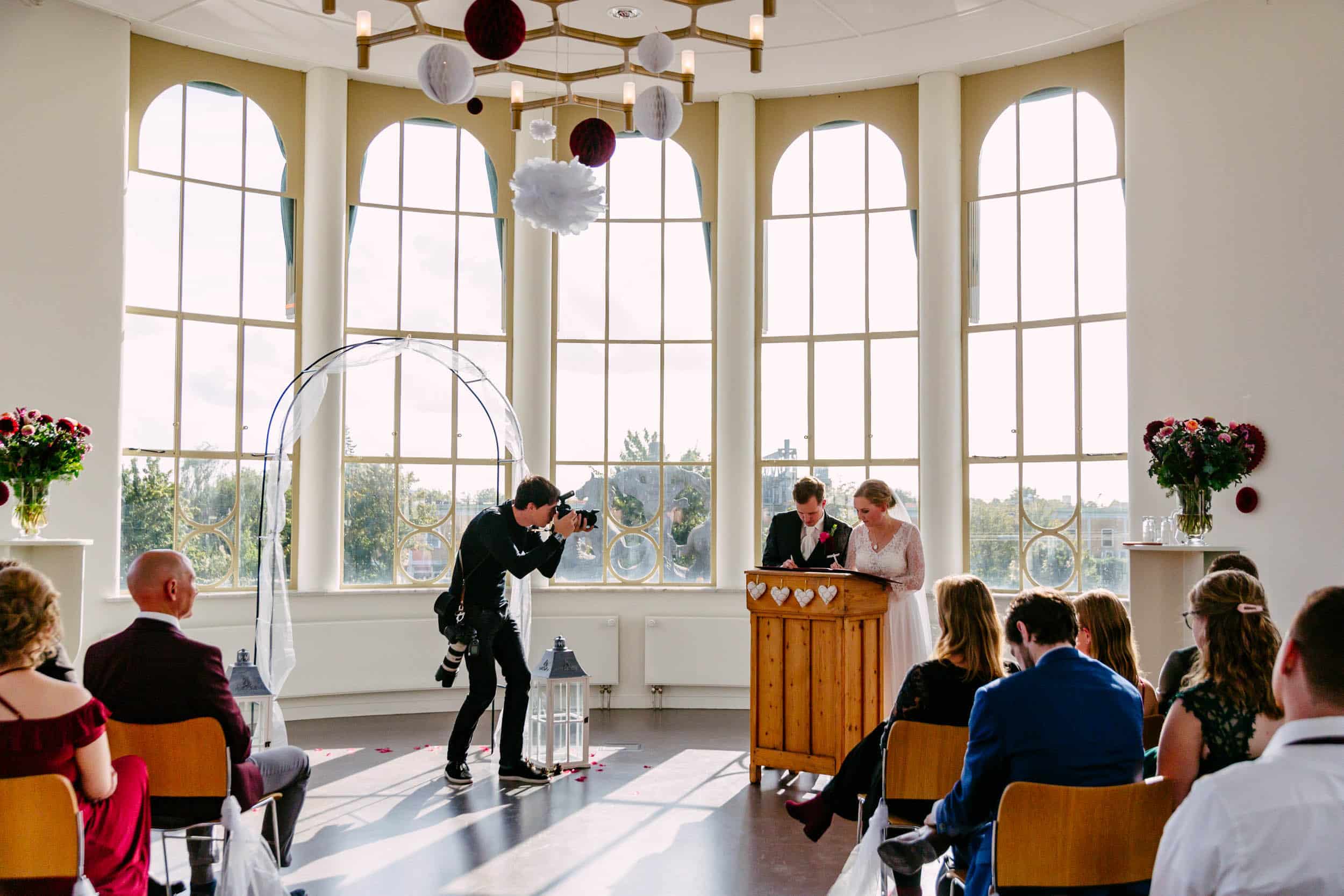 Een huwelijksceremonie in een kamer met grote ramen, voorzien van Huwelijkse Voorwaarden.
