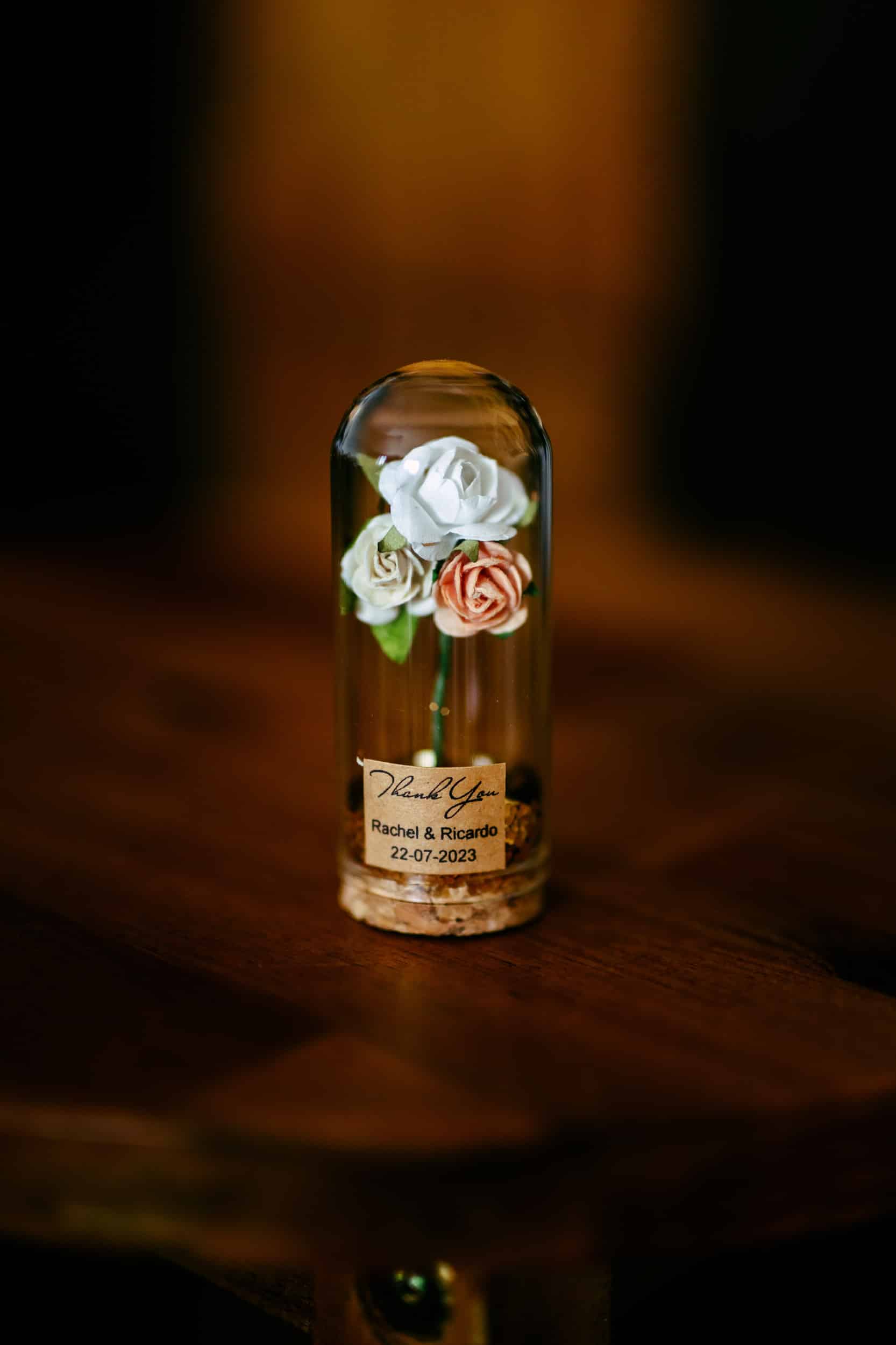 Een roos in een glazen fles op een houten tafel, dienend als charmant en elegant bedankje voor de geliefde gasten.
