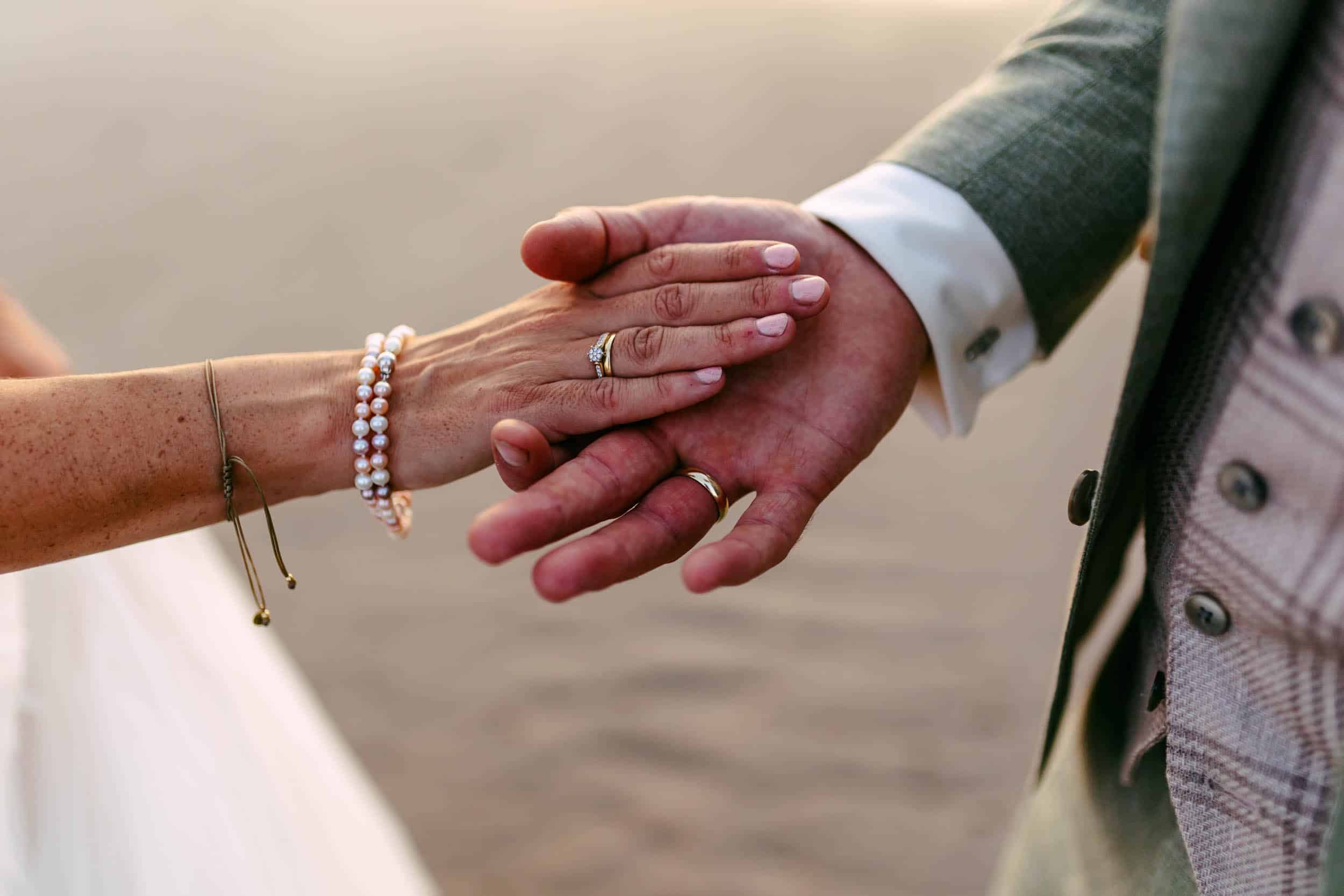 Een betoverend moment van een bruid en bruidegom die elkaars hand vasthouden op een pittoresk strand en de essentie van liefde en huwelijk vastlegt.