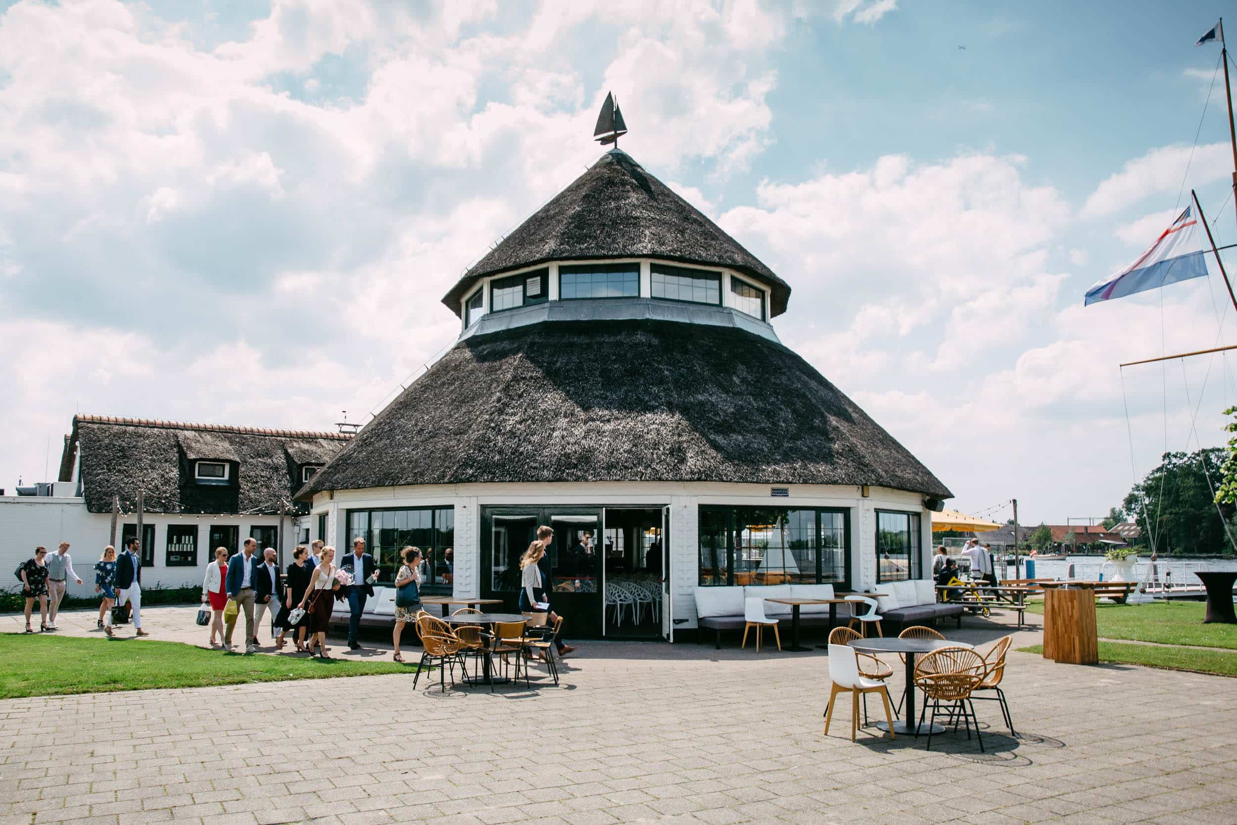 Waterlust the Kaagsociëteit is a restaurant with a thatched roof and tables outside.
