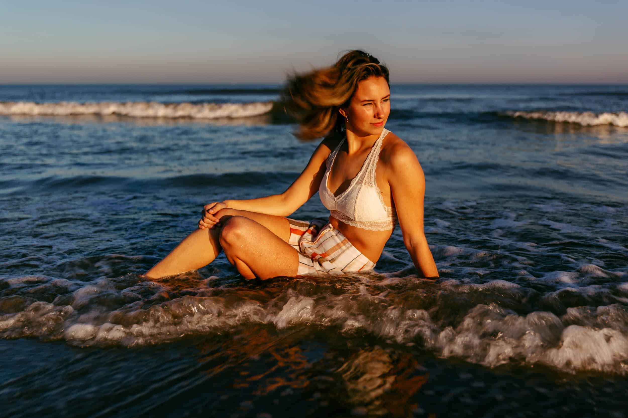 A woman poses for a photo shoot on the beach surrounded by the ocean.