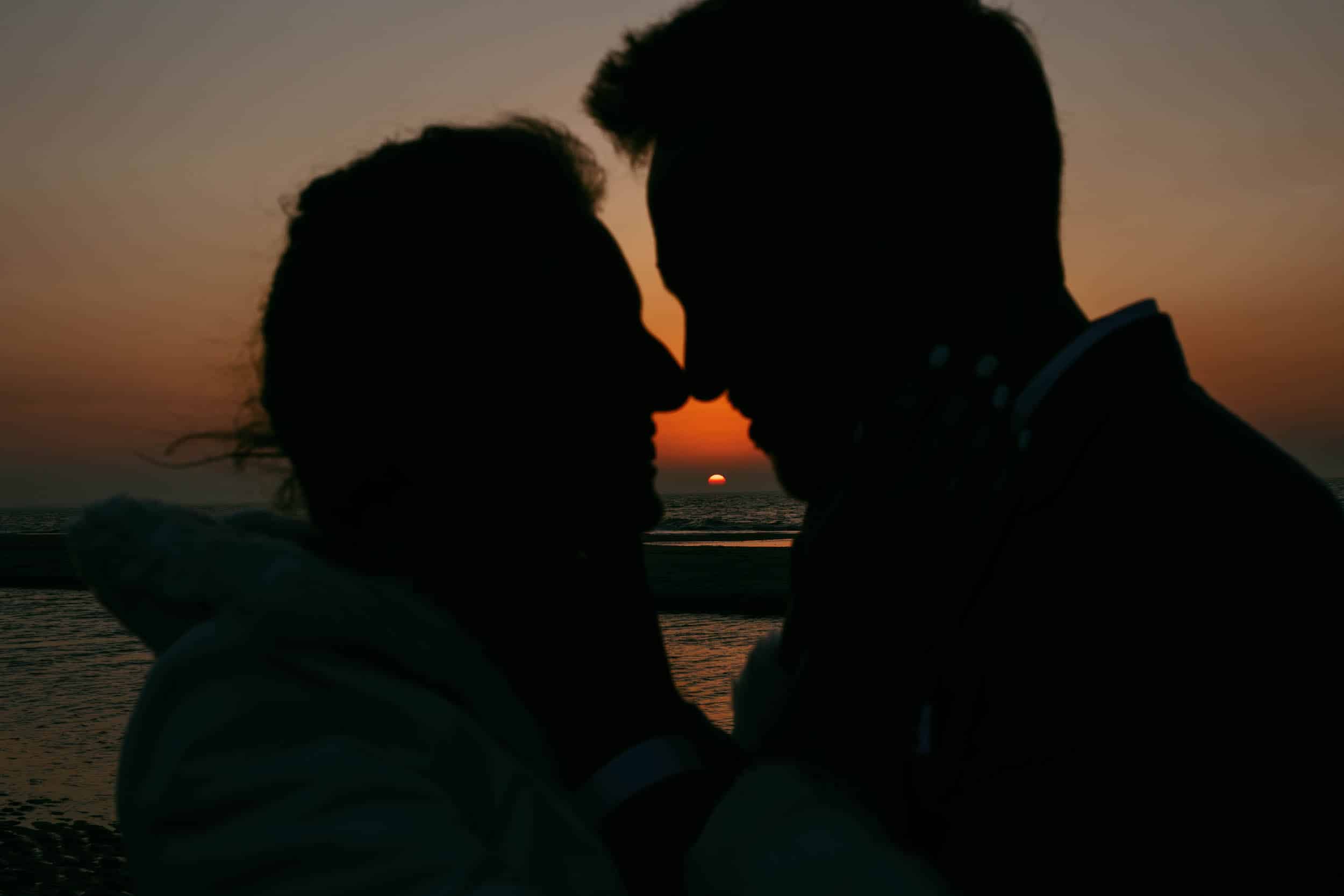 Een silhouet van een kussend koppel op het strand tijdens zonsondergang, waarbij de serene en romantische strandelementen worden vastgelegd.