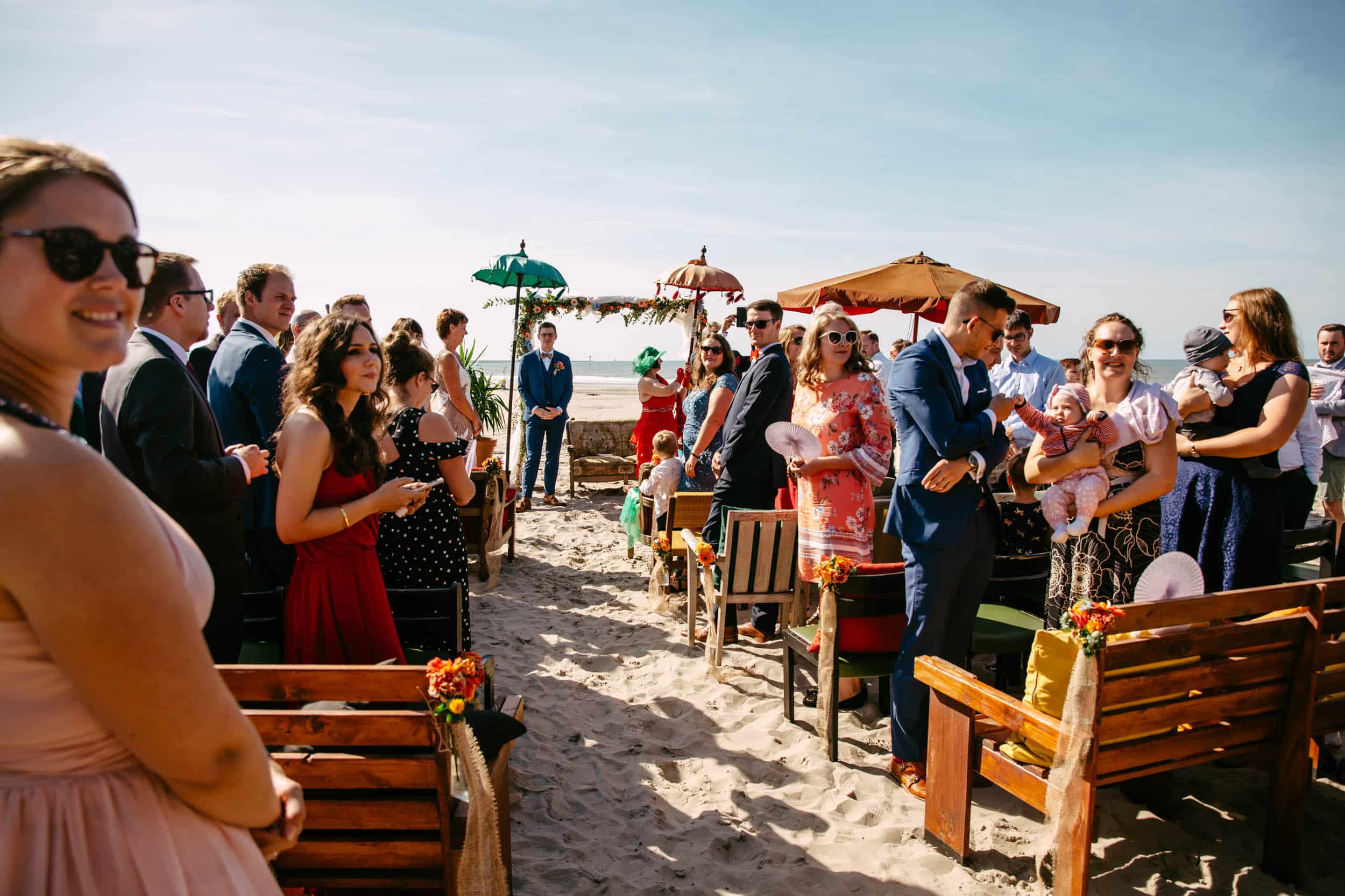 Een strandhuwelijksceremonie waar veel mensen naar kijken.