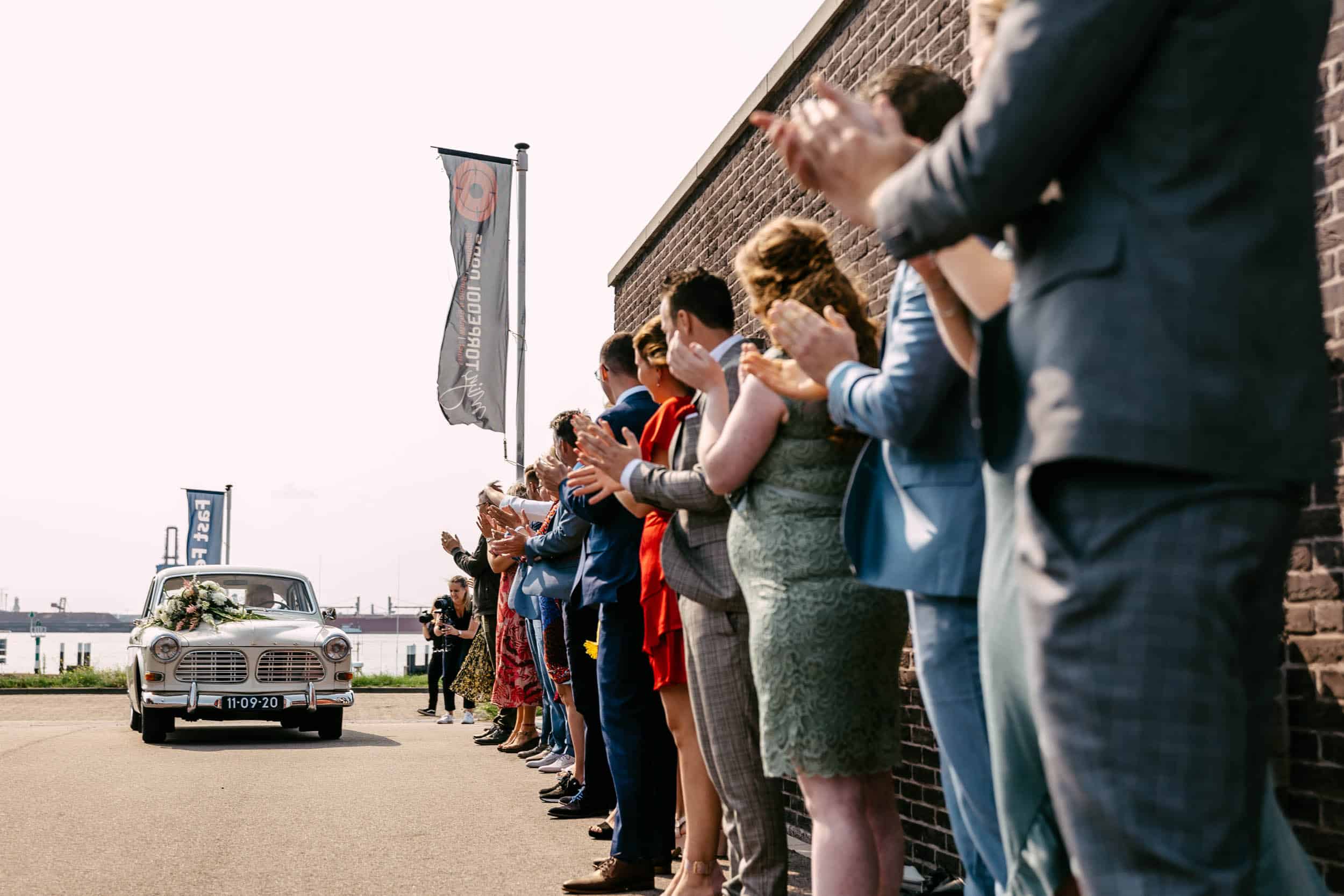 A group of people clap in front of a car.
