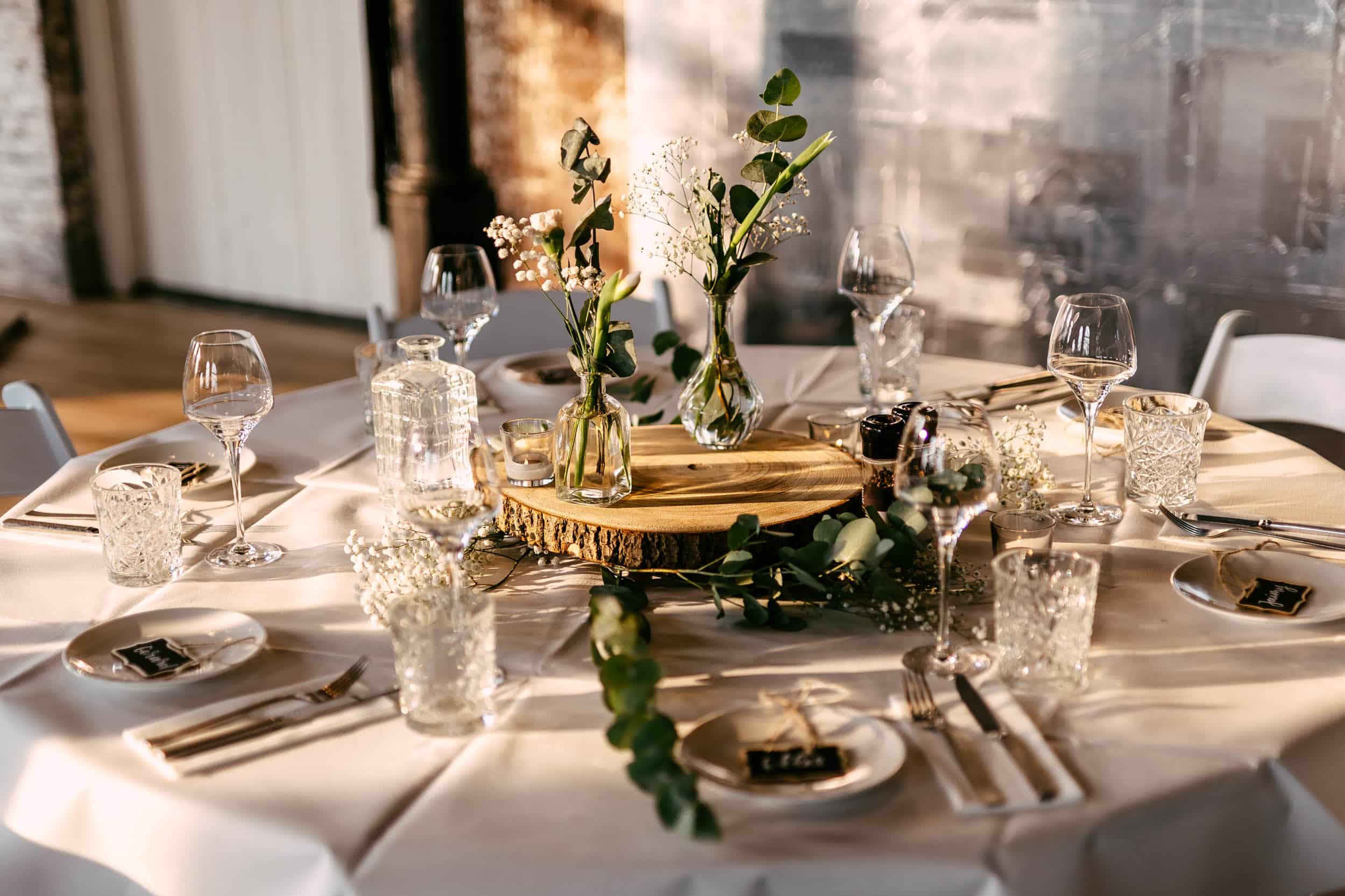 A table setting with white plates, glasses and greenery.