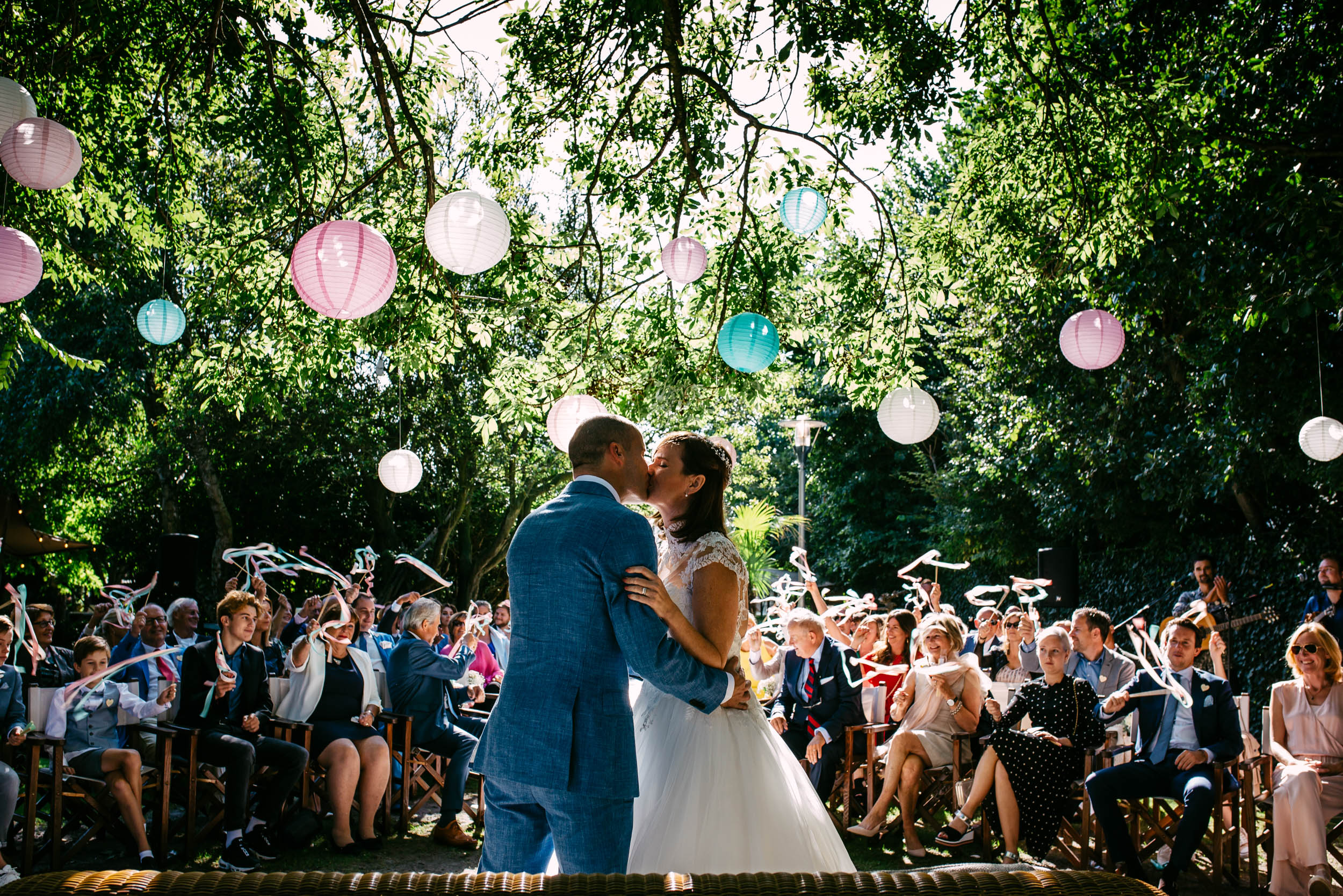 A bride and groom share a romantic kiss in front of a crowd at De Viersprong, S Gravenzande.