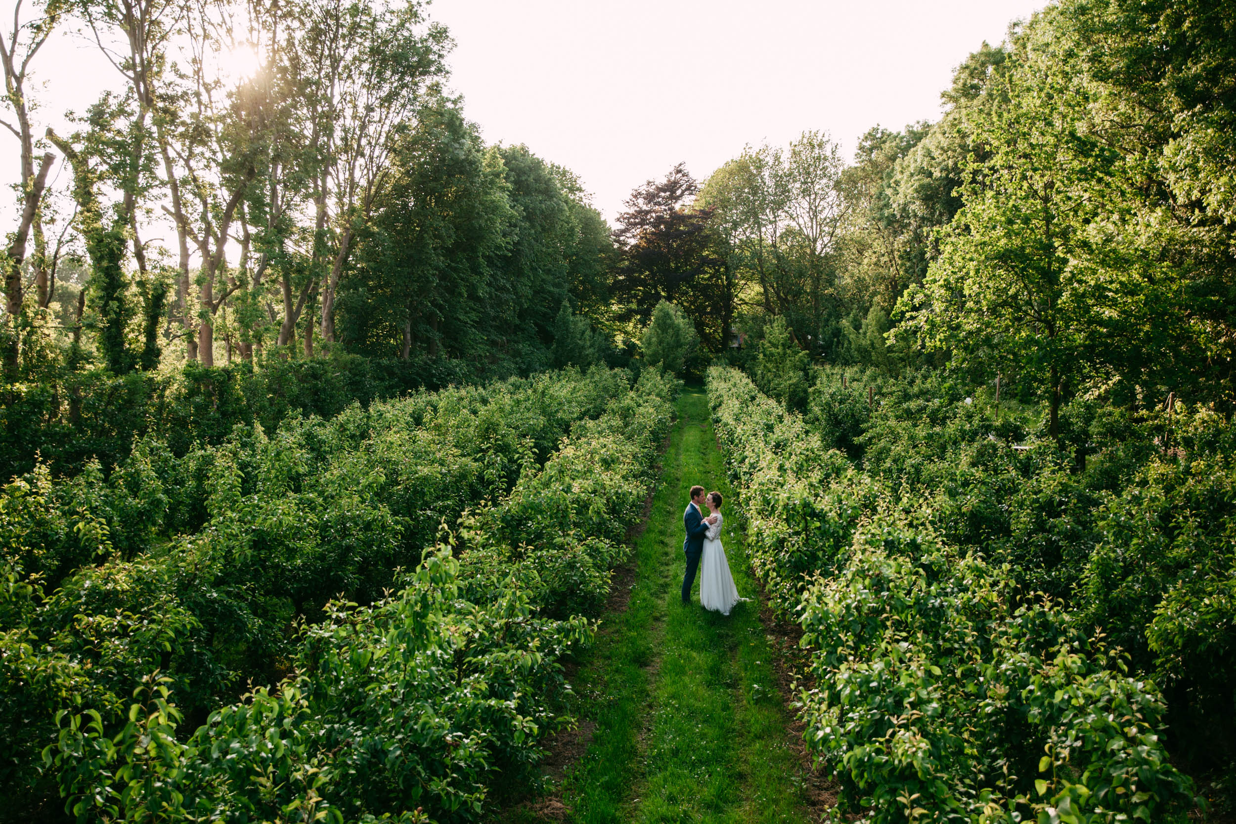 Een bruid en bruidegom wandelen door Landgoed de Olmenhorst, een betoverende boomgaard.