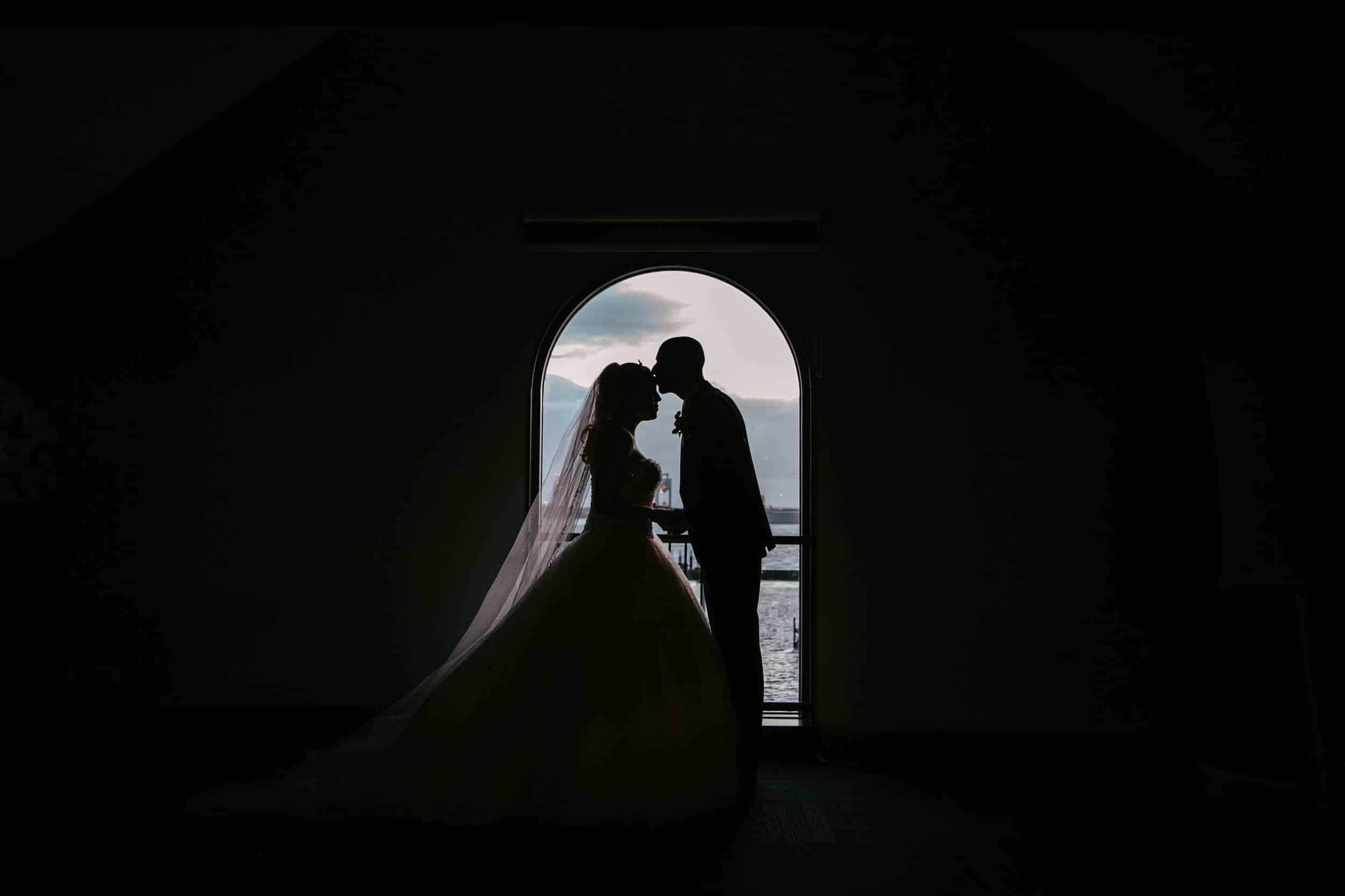 Een silhouet van een bruid en bruidegom die voor een raam bij Mijn torpedoloods staan.
