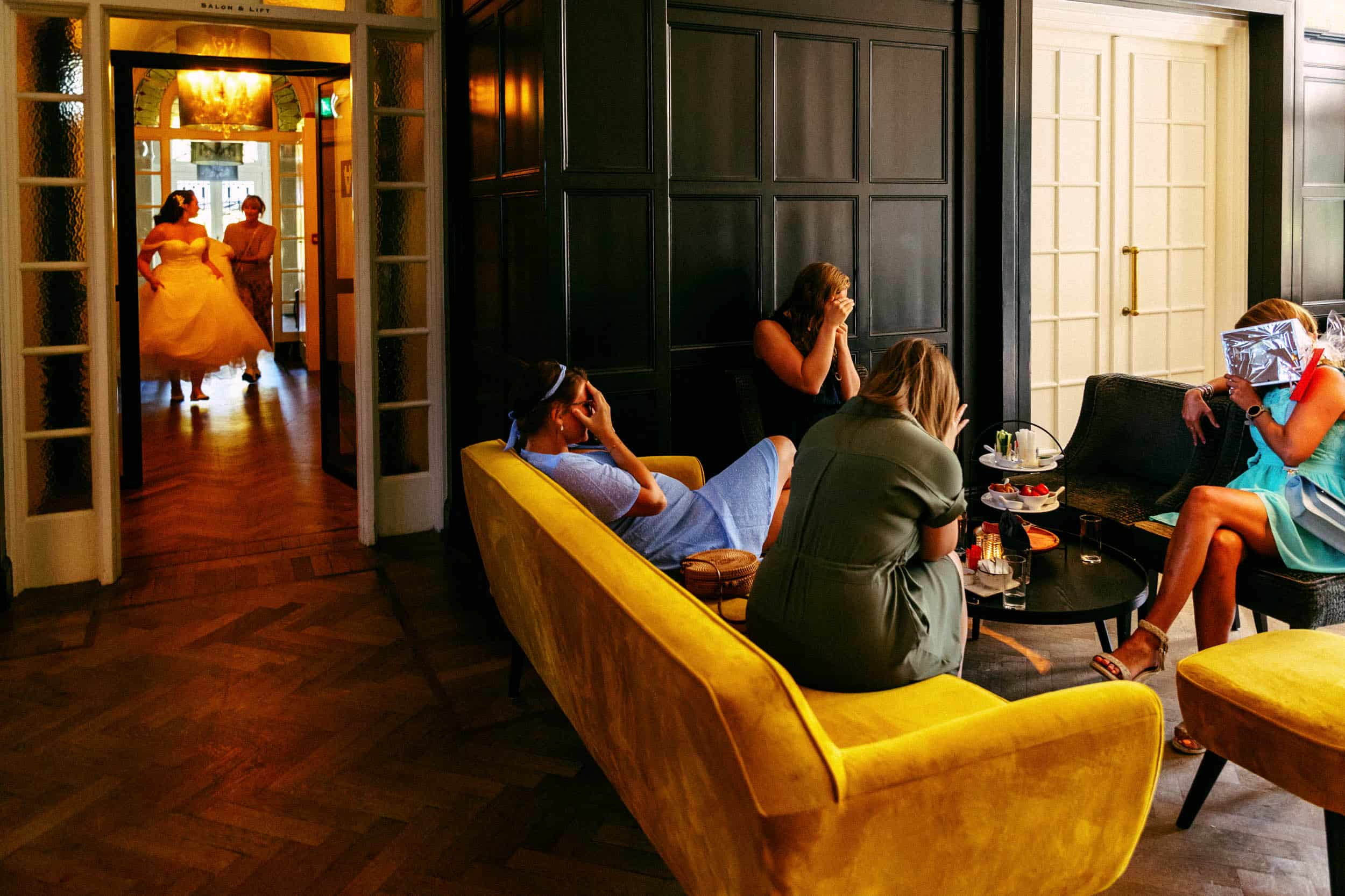A group of people sit on yellow couches in a room.