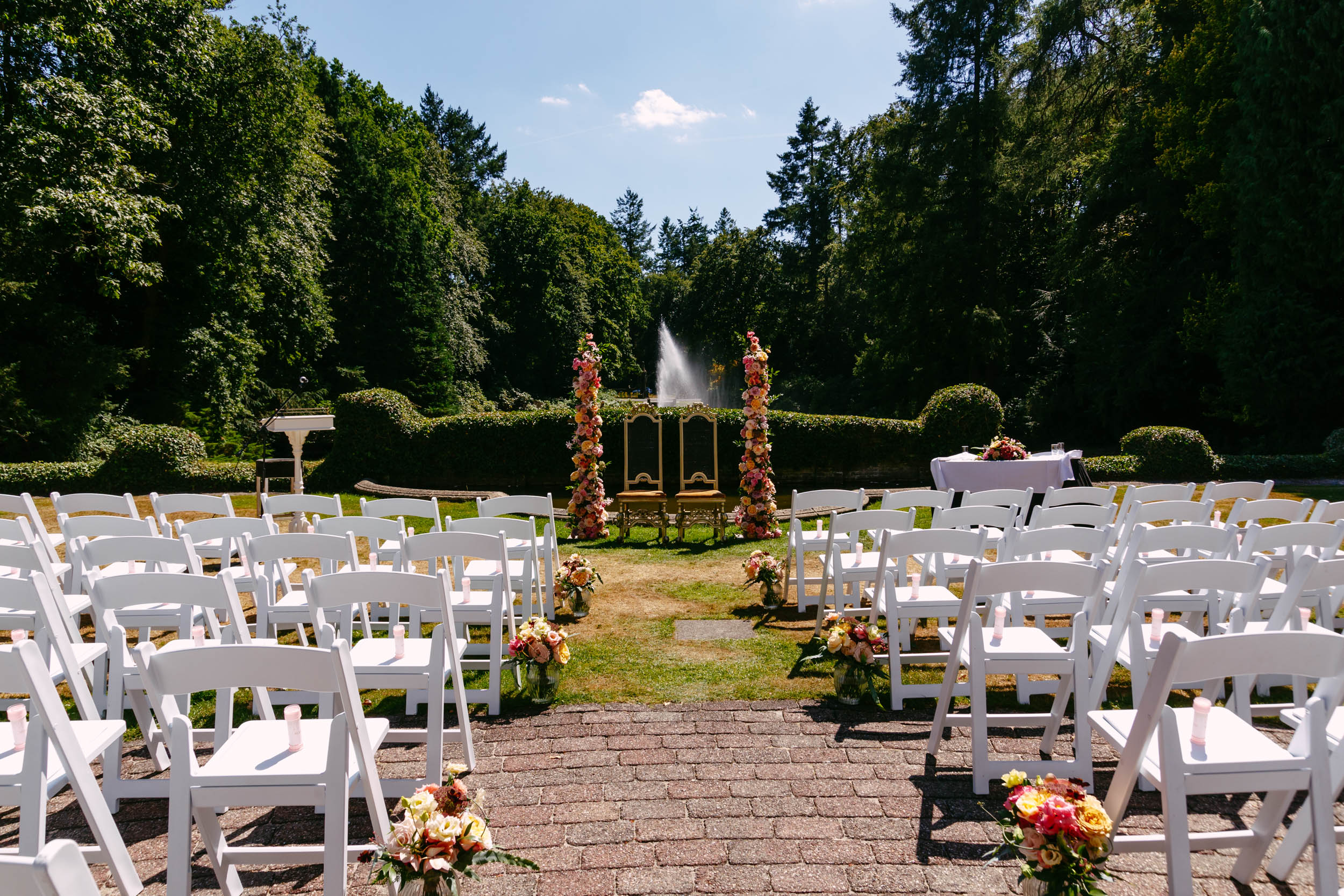 An outdoor wedding ceremony with white chairs and a fountain.