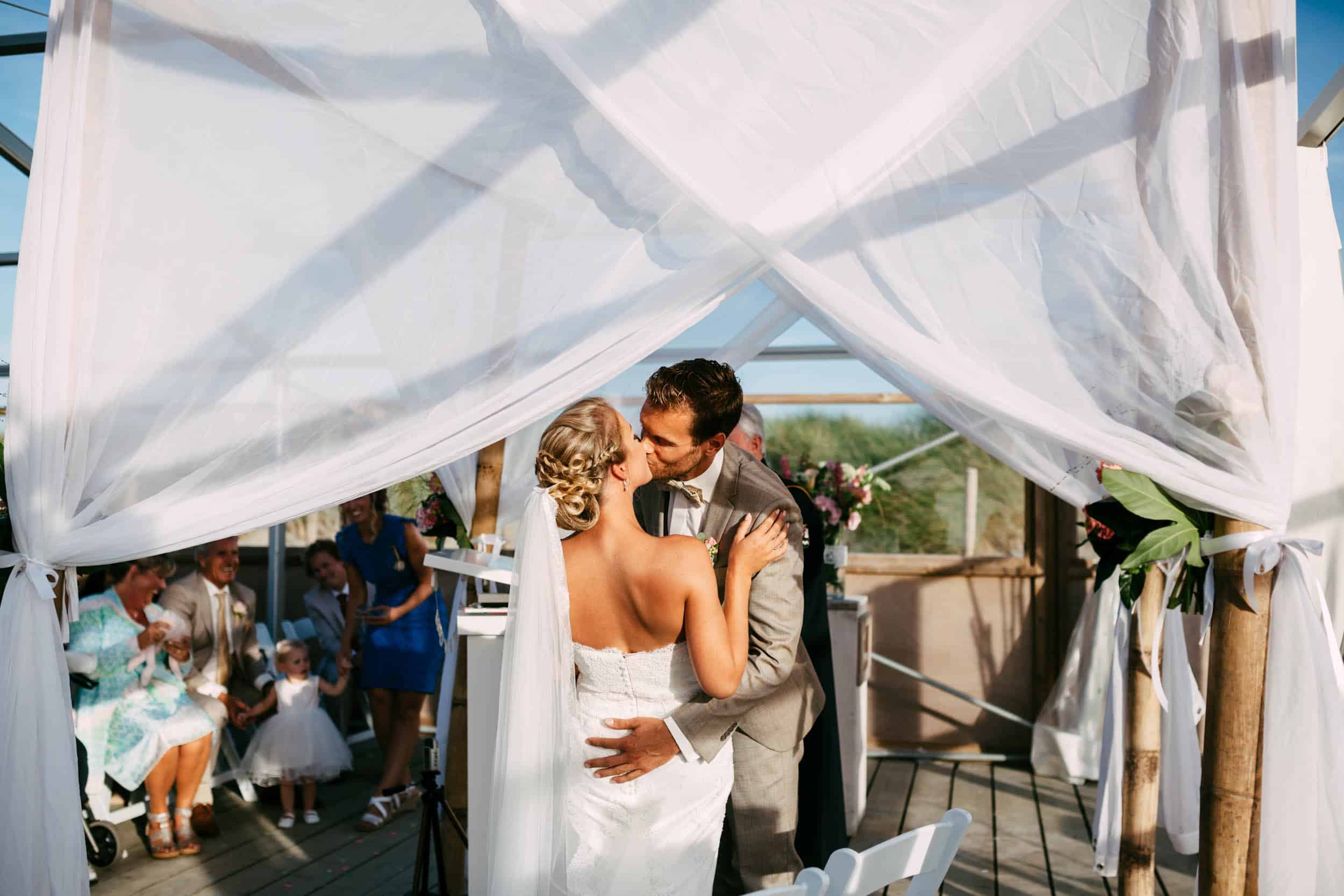 Een bruid en bruidegom kussen elkaar onder een tent tijdens hun huwelijksceremonie.