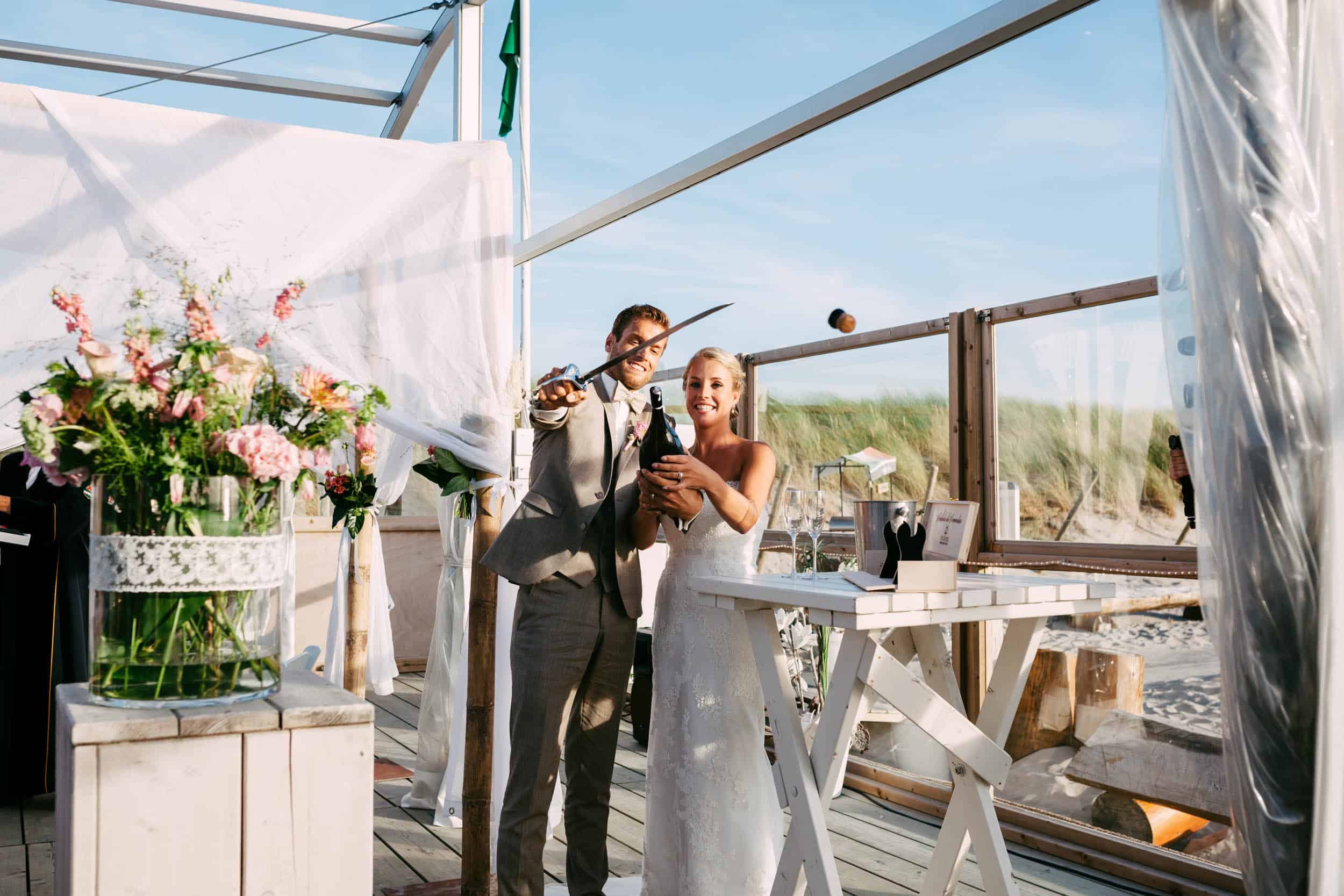 A bride and groom stand in front of a tent on the beach.