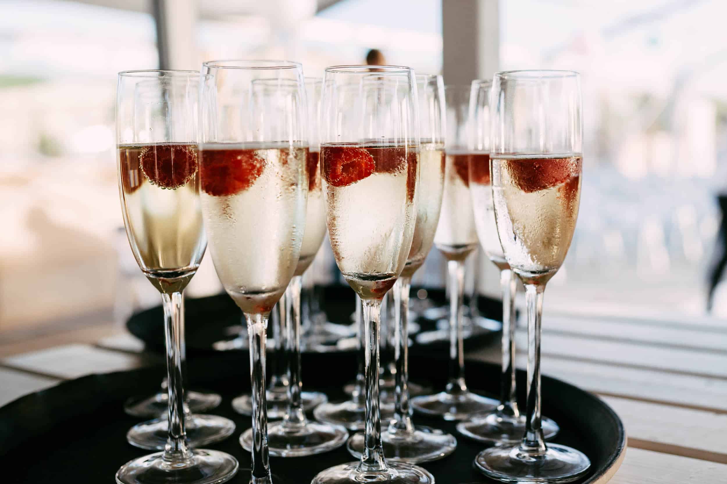Champagne flutes with raspberries on a tray.