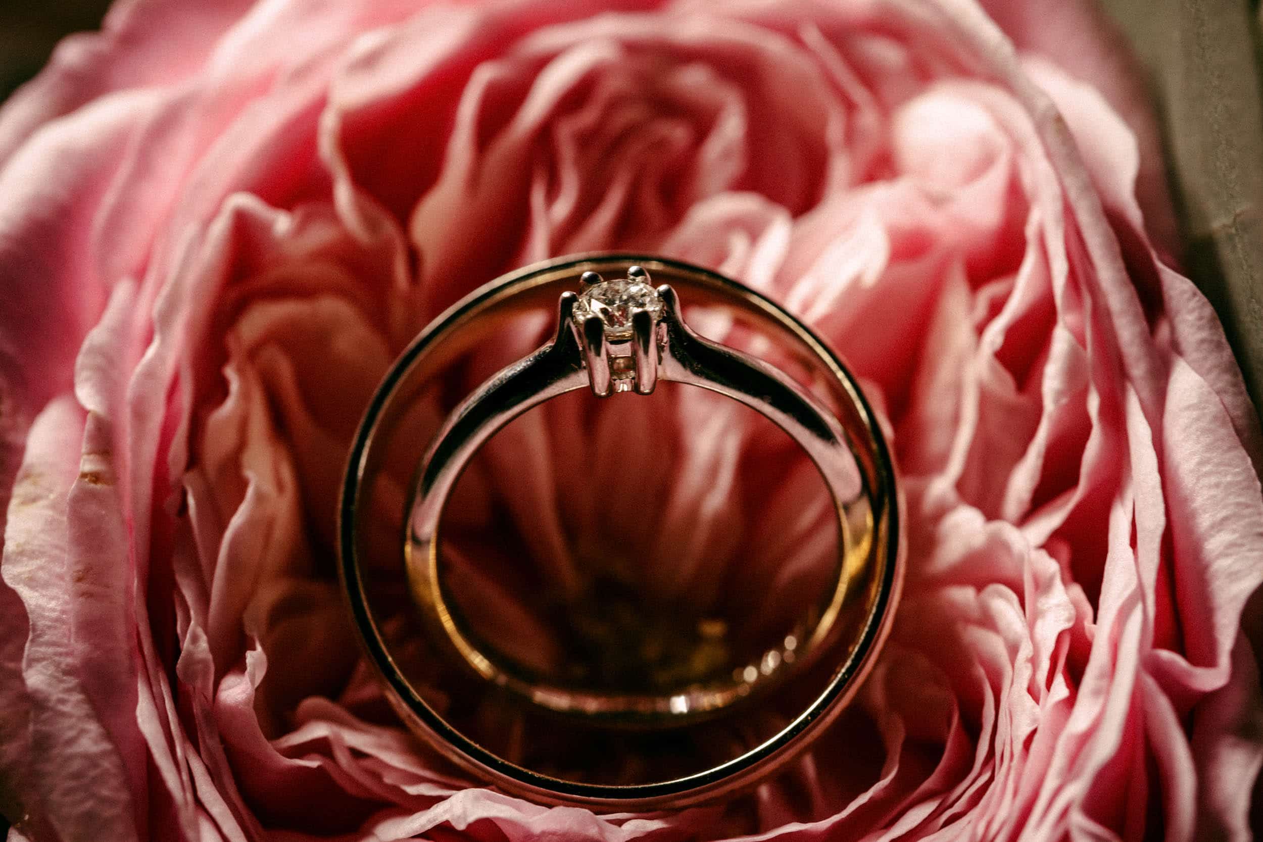 De perfecte bruiloft wordt vastgelegd op een Trouwfoto met een verlovingsring die elegant op een roze bloem rust.