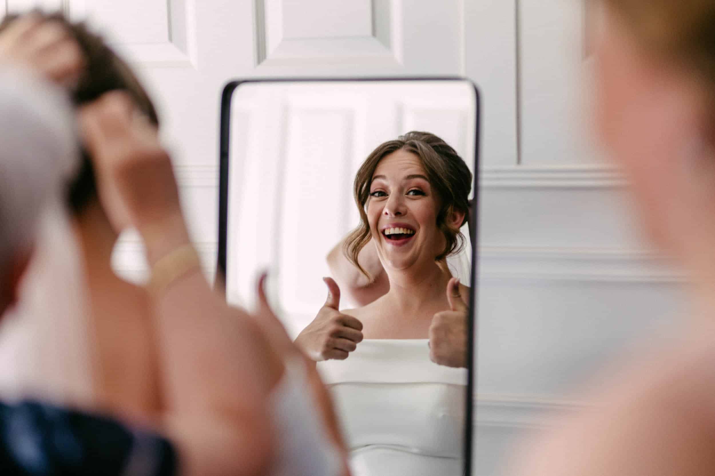Een bruid die een duim omhoog steekt voor een spiegel op haar perfecte trouwdag, vastgelegd door de trouwfotograaf.