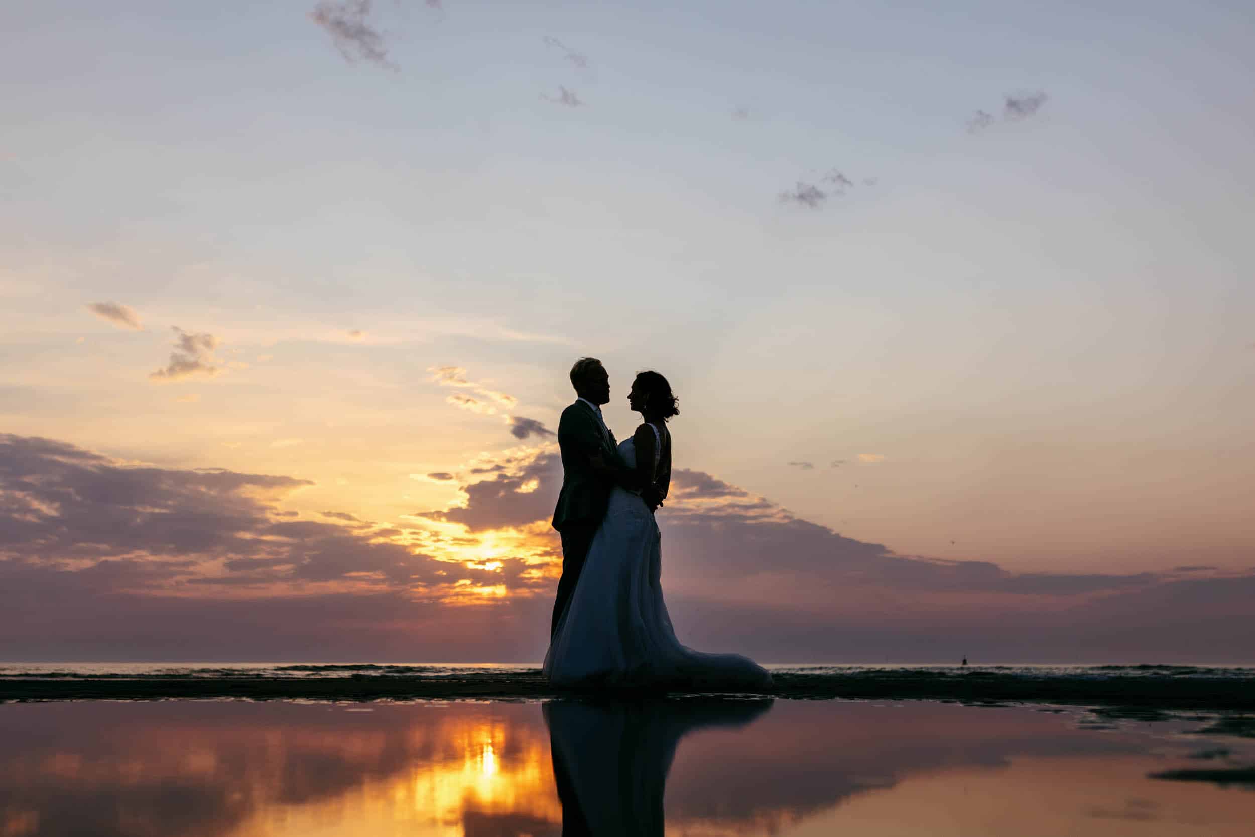 A bride and groom enjoy a romantic photo shoot in the water at sunset for the perfect wedding.
