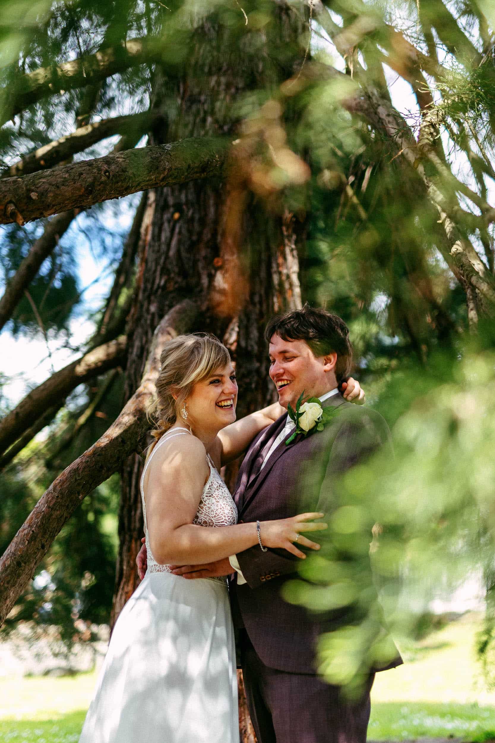 A bride and groom cuddling in front of a tree during their perfect wedding day.