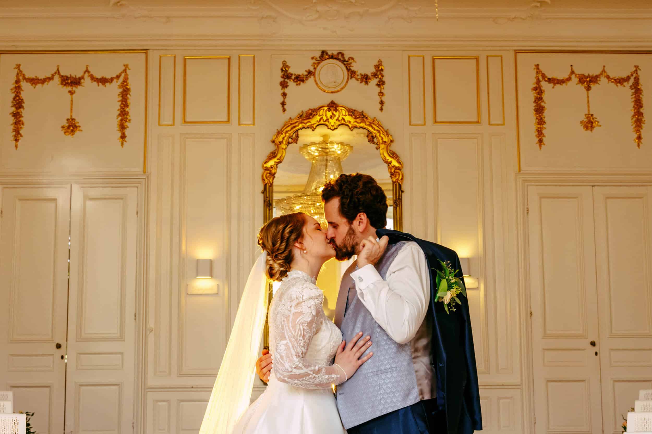 "Een bruid en bruidegom die een hartstochtelijke kus delen in een sierlijke kamer, prachtig vastgelegd door een trouwfotograaf. Deze trouwfoto geeft perfect de essentie van de perfecte bruiloft weer