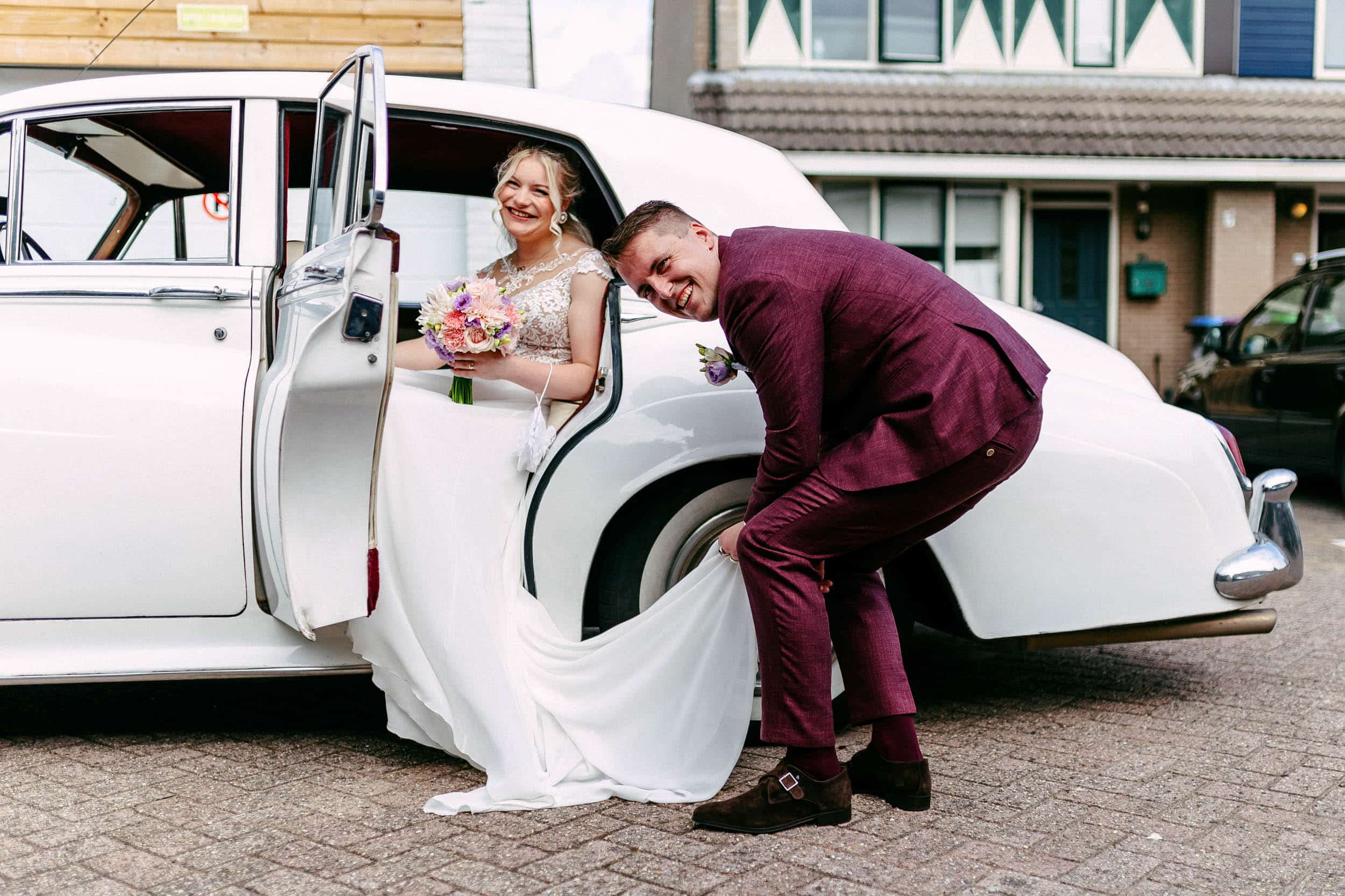 A bride and groom leaning against the door of a vintage car.