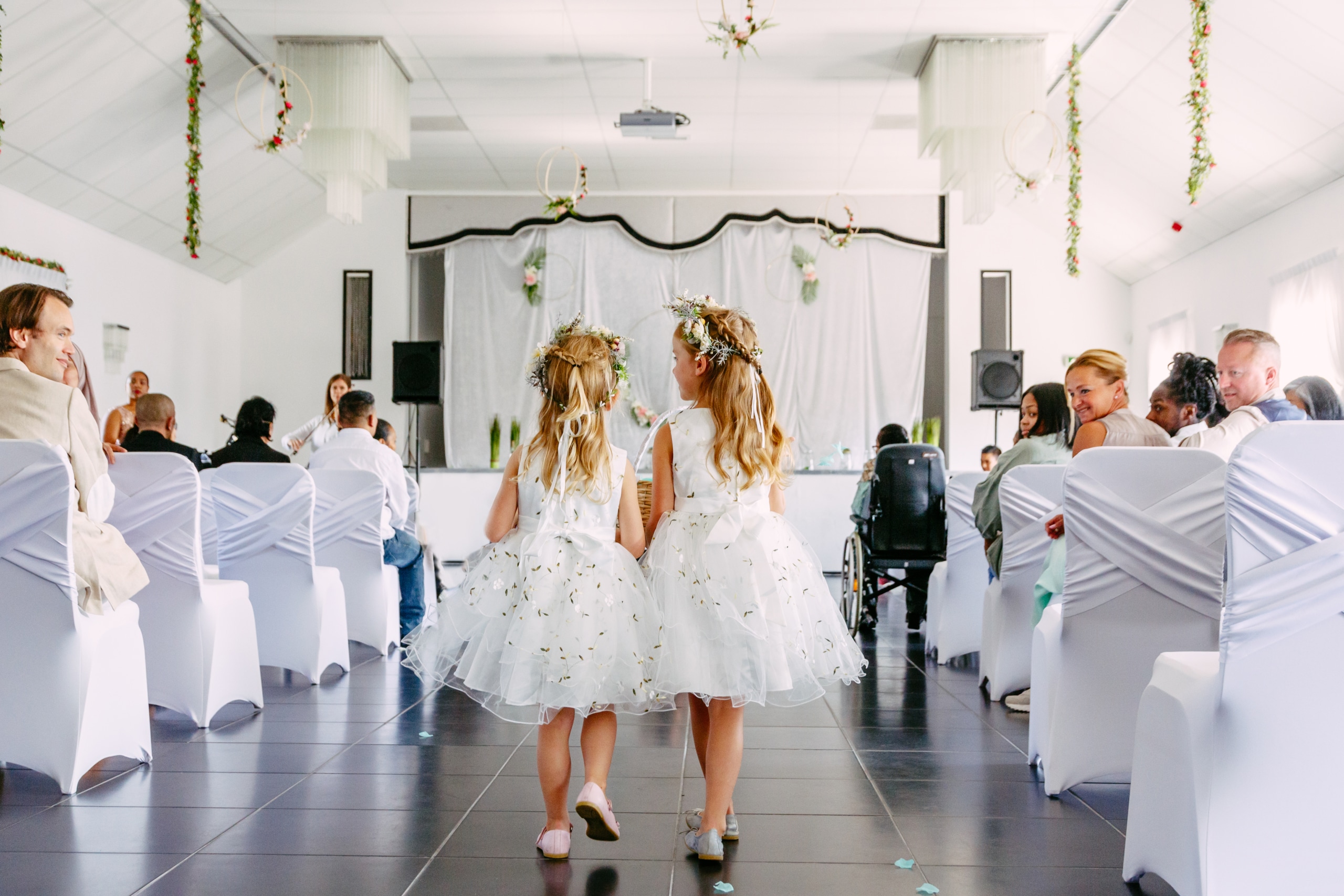 Twee meisjes in witte jurken lopen door een gangpad.